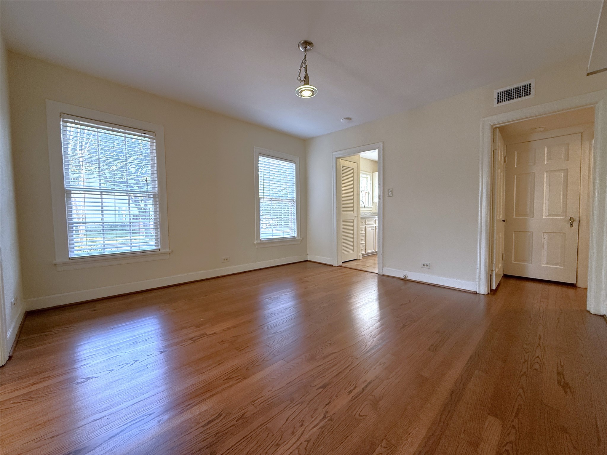 Alternate view of the dining room, natural light flows in from twin windows. A privacy door opens into the hallway leading to the bedrooms and baths.