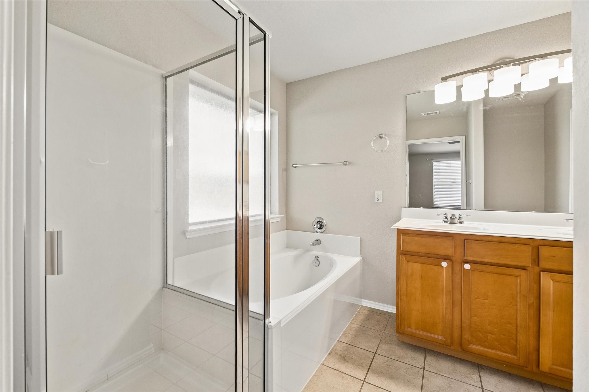 Private primary bathroom featuring dual sinks, soaking tub, separate glass-enclosed shower, and generous vanity storage.