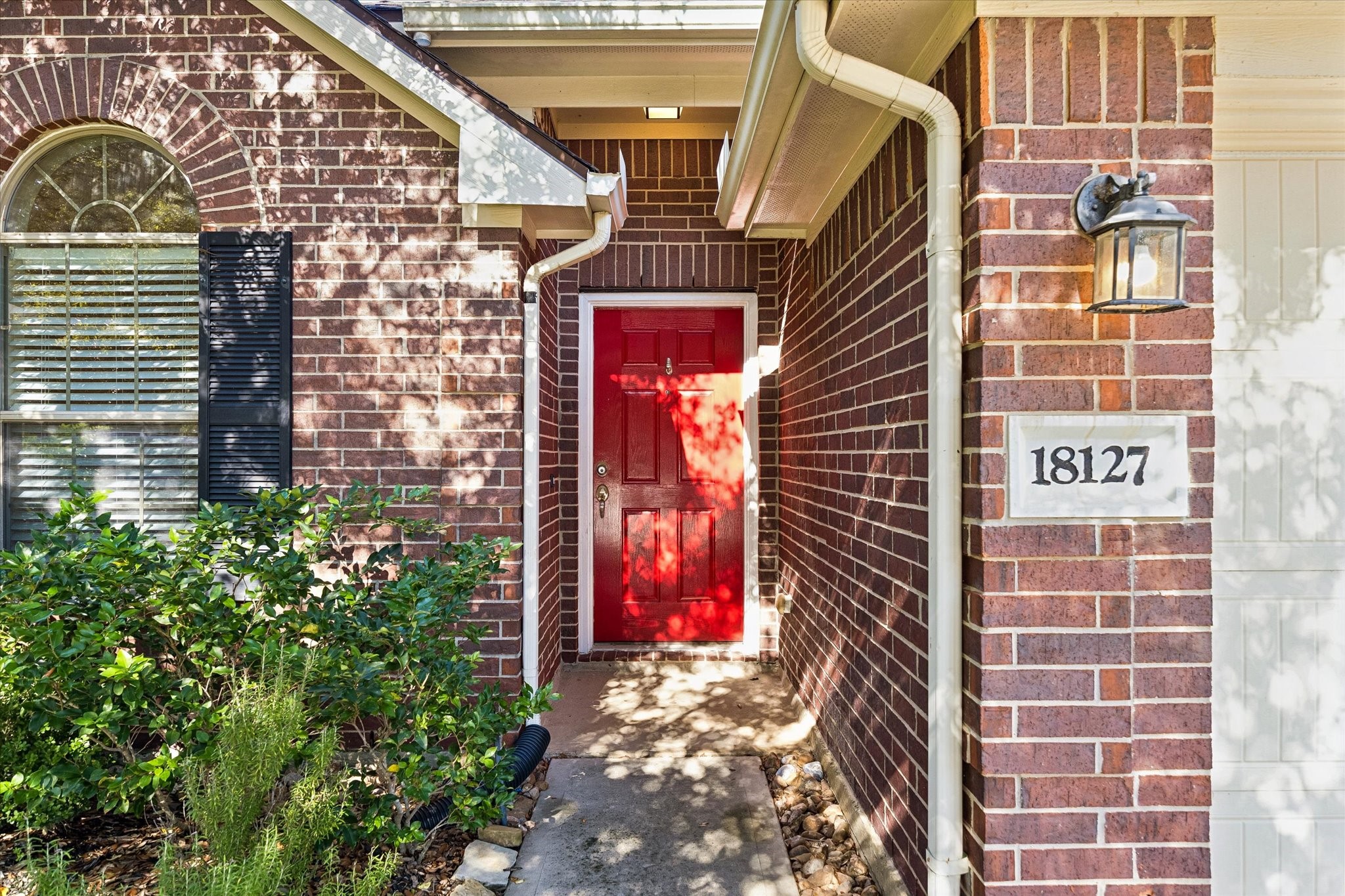 Inviting covered front entry with a cheerful red front door, decorative shutters, and established landscaping.