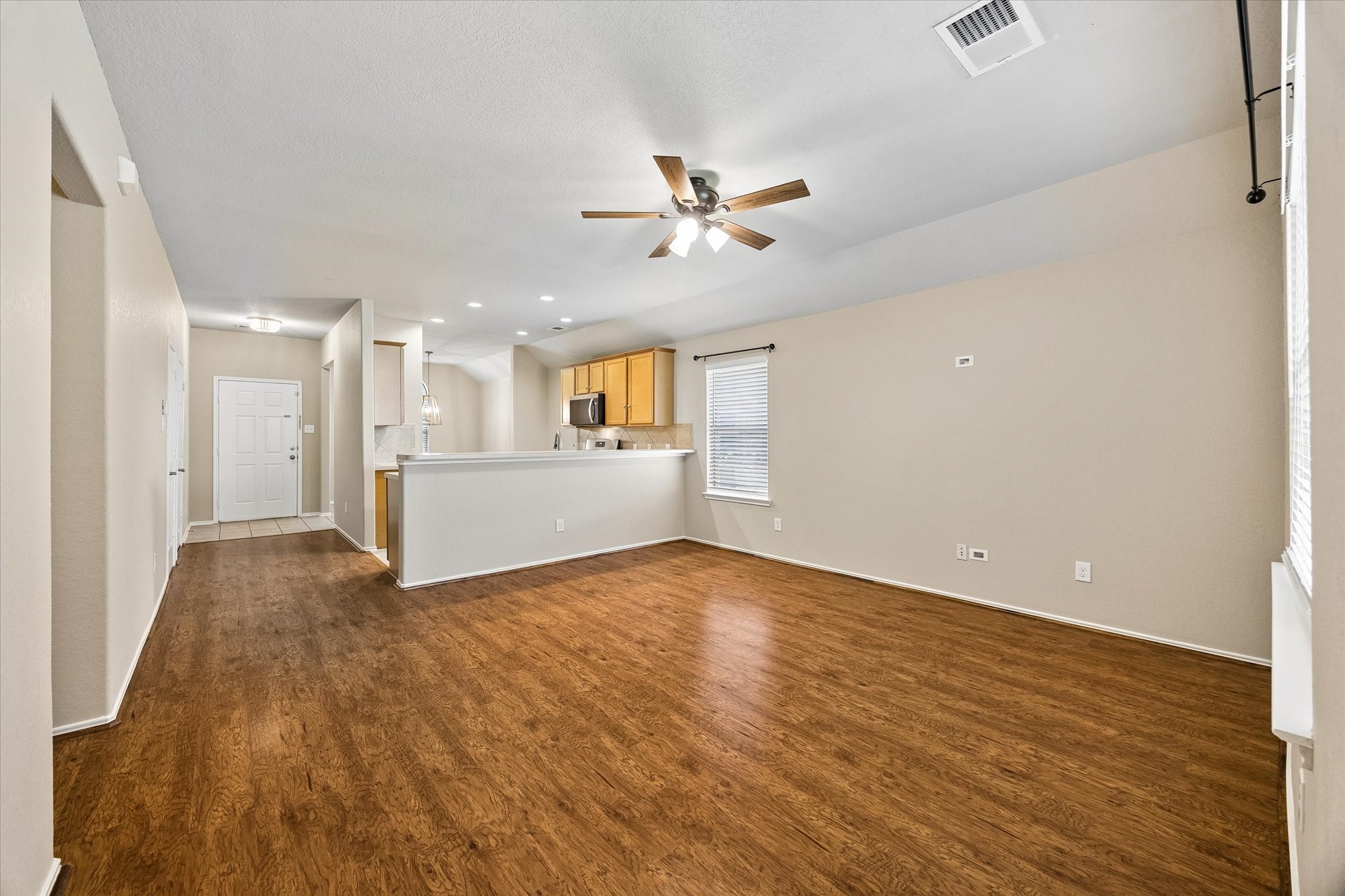 Open living area featuring wood-look flooring, fresh paint, and a breakfast bar overlooking the main gathering space.