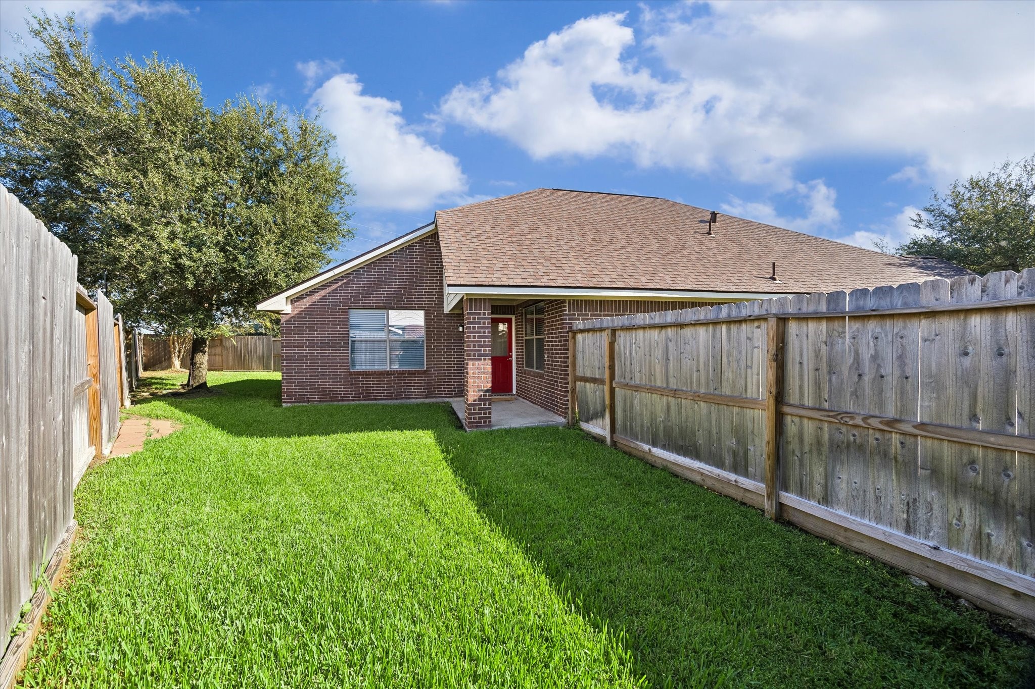 Rear view of the home showcasing the brick exterior, covered back patio, and fenced backyard.