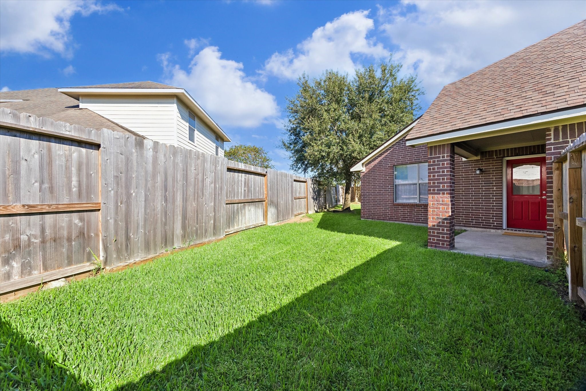 Fenced backyard featuring a grassy lawn and mature shade tree, offering space for gardening, outdoor activities, or entertaining.