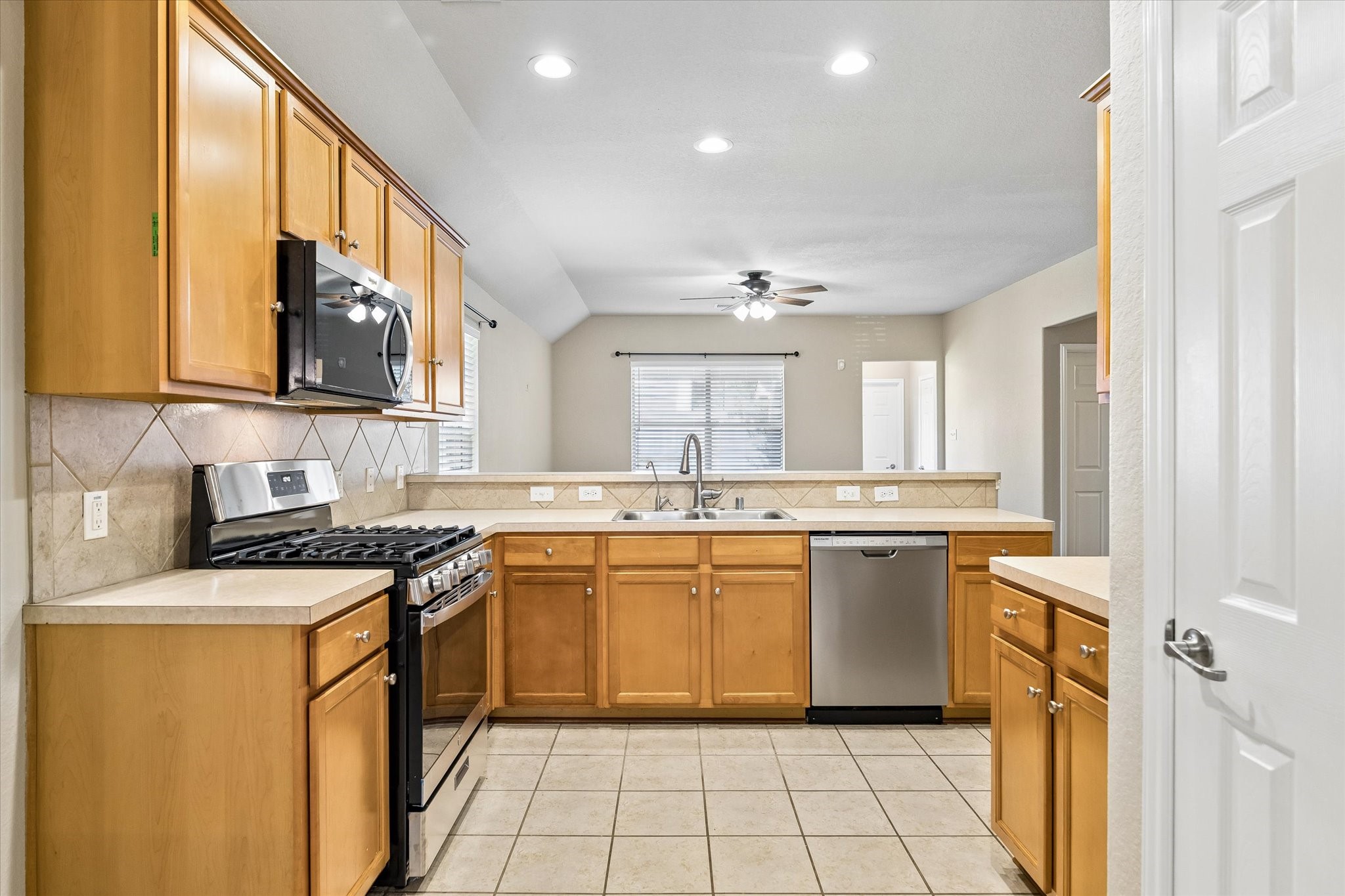 Functional kitchen featuring a NEW gas range, stainless steel dishwasher, tile backsplash, ample cabinet storage, and breakfast bar.