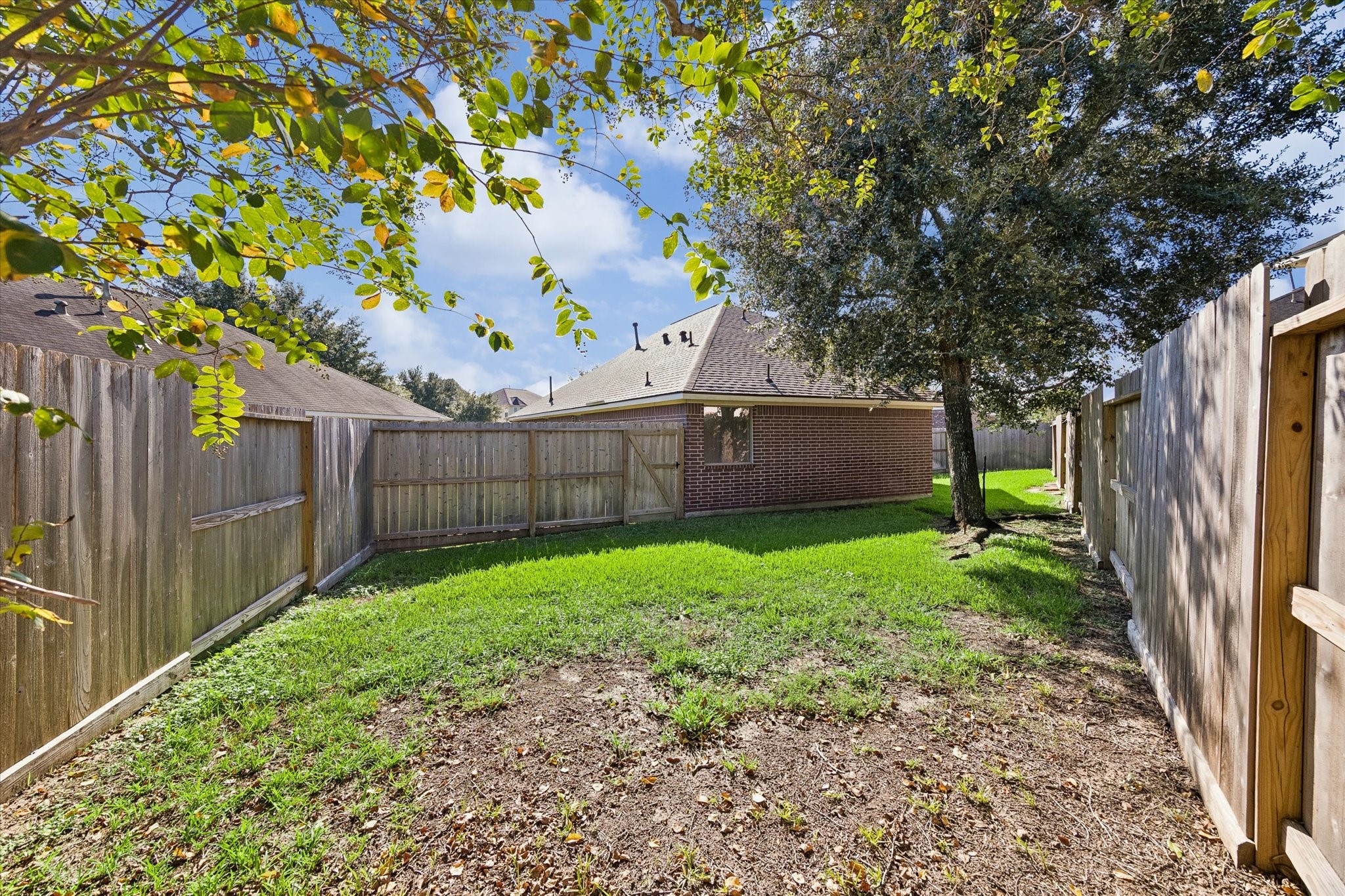 Additional view of the fenced backyard featuring mature trees, open green space, and covered patio.