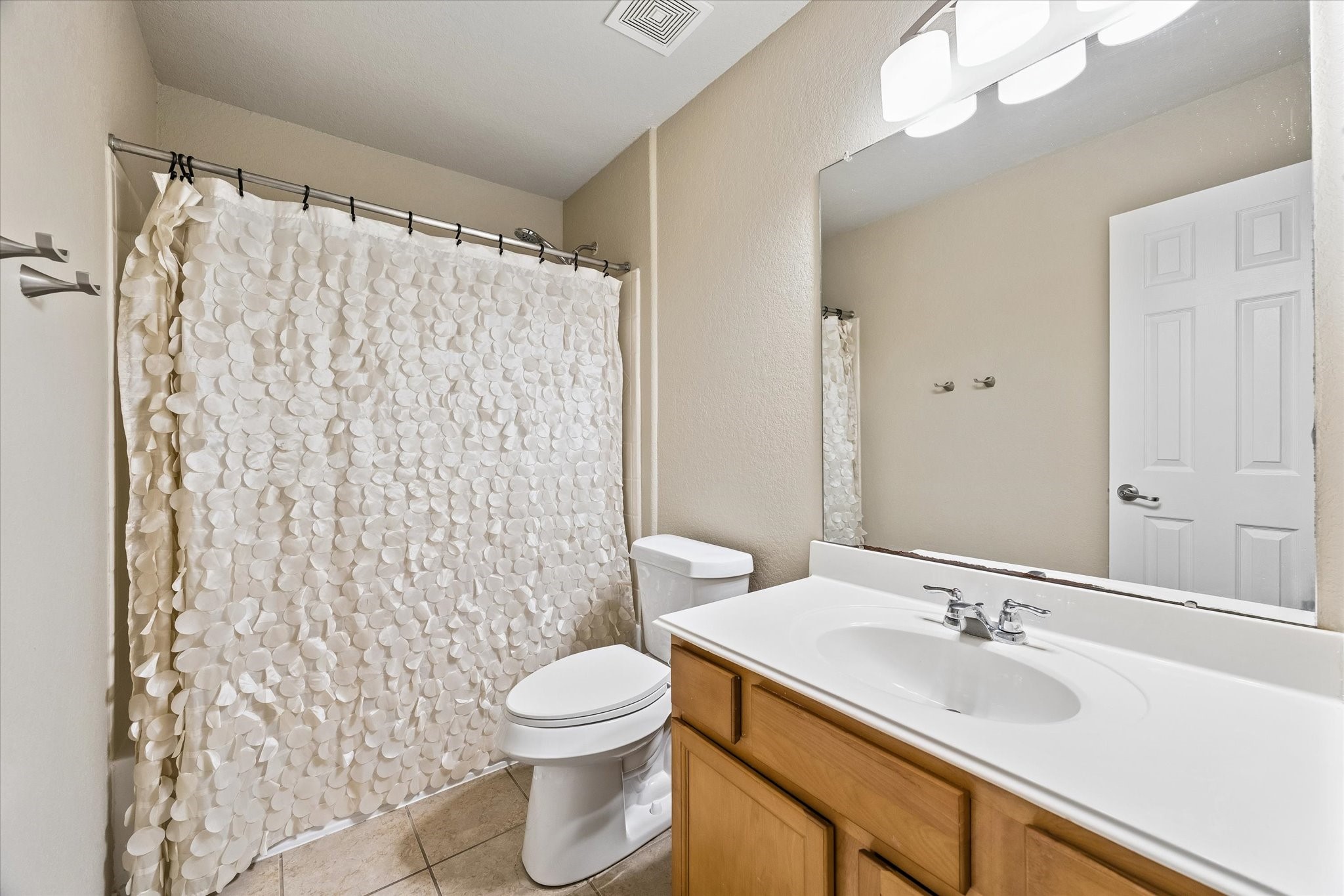 Secondary bathroom featuring a tub and shower combination, single-sink vanity, and tile flooring.