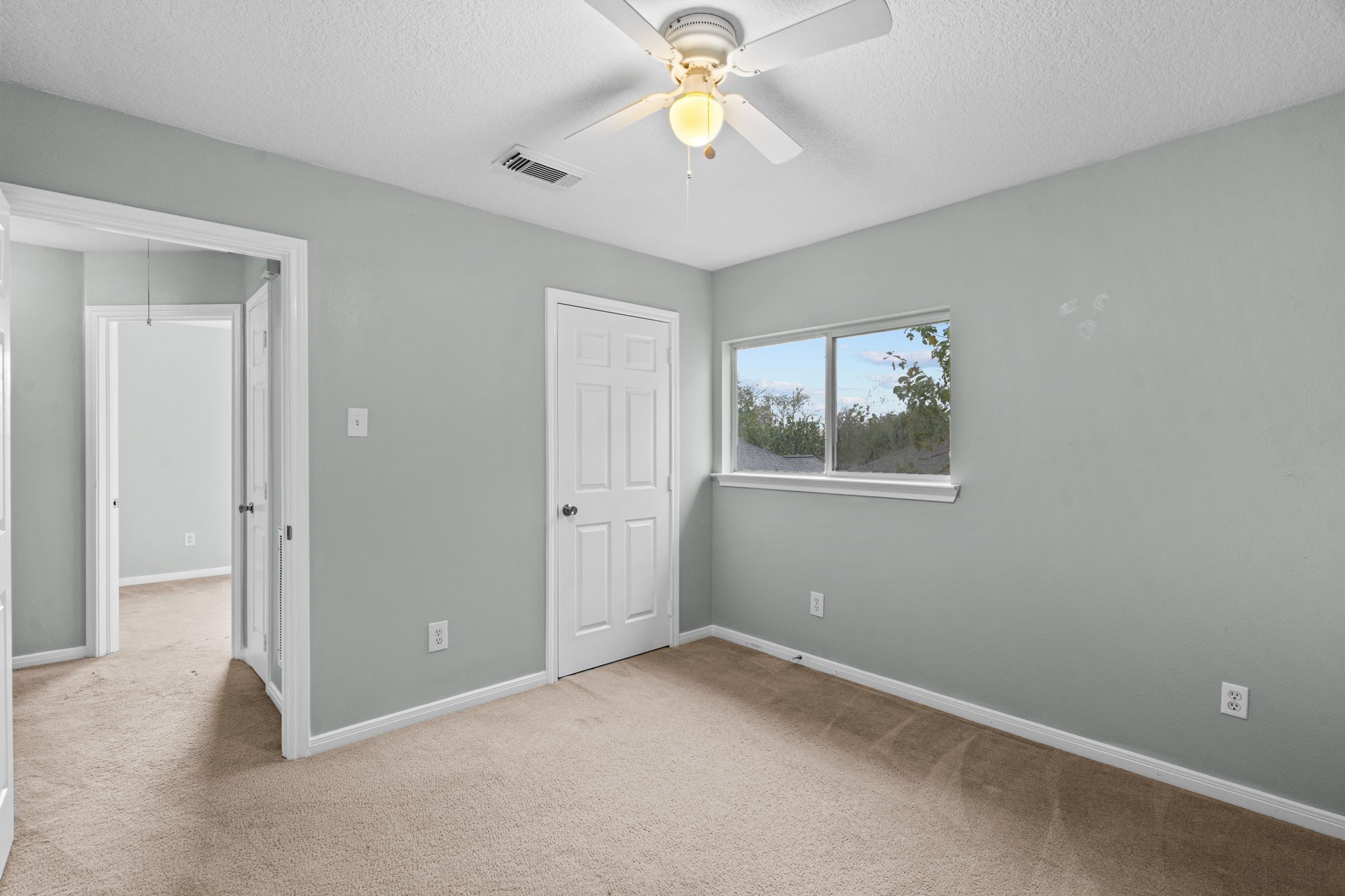 Bright and cozy bedroom with soft gray walls, plush carpeting, and a ceiling fan.