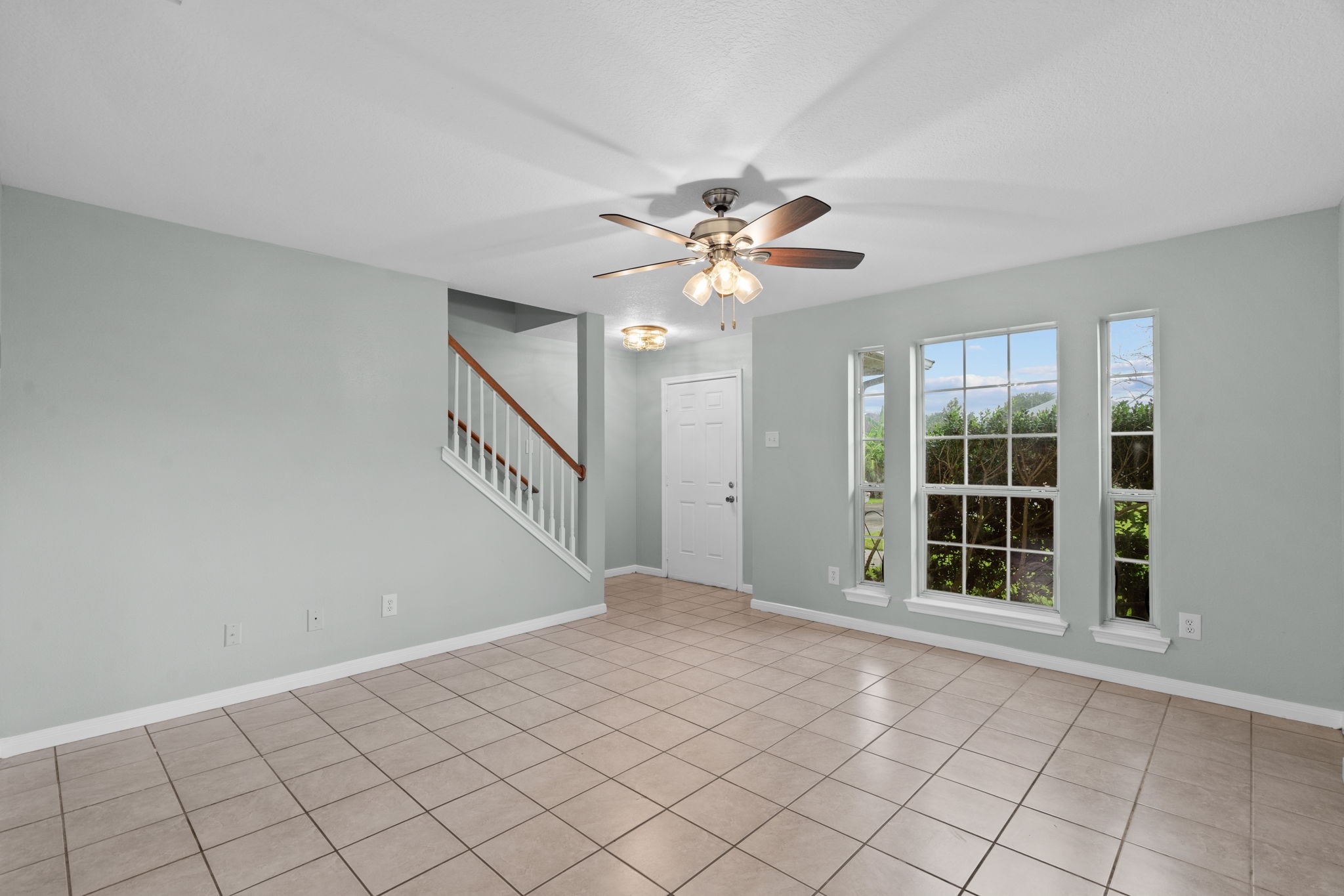 Bright living area with large windows, neutral tile flooring, and a ceiling fan.