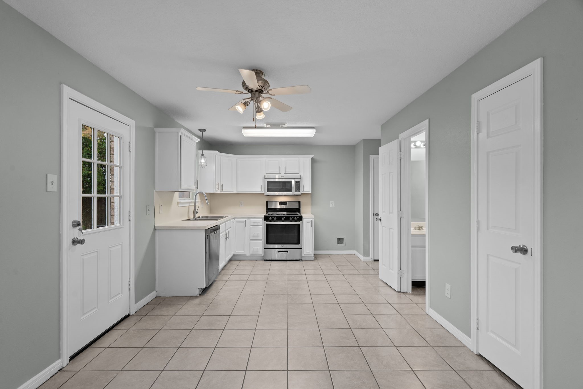 Bright and spacious kitchen with modern stainless steel appliances, ample white cabinetry, and a convenient tile floor.