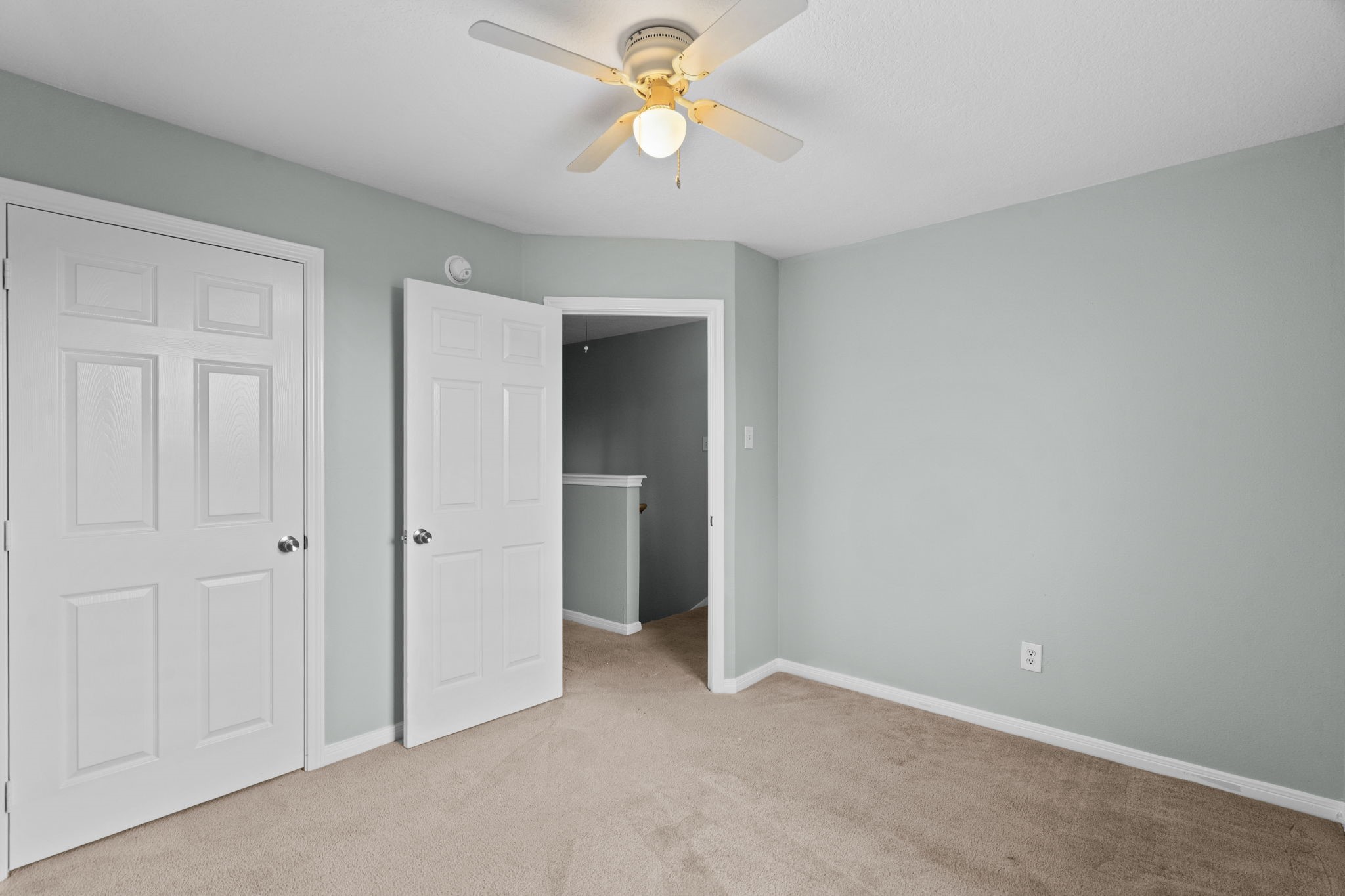 Bright and inviting bedroom featuring soft carpet, calming gray walls, and a ceiling fan for comfort.