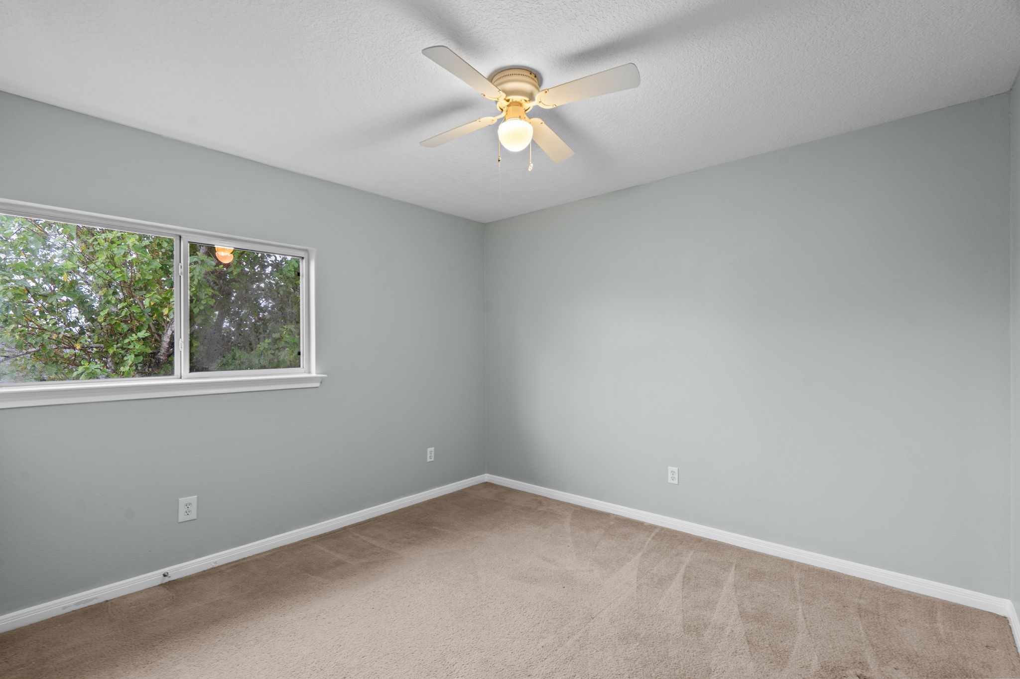 Bright and cozy bedroom with soft gray walls, plush carpeting, and a ceiling fan.