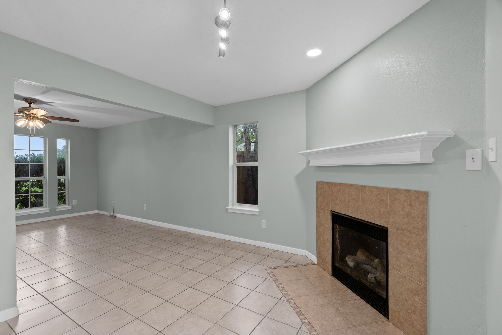 Spacious living area features elegant tile flooring, a cozy fireplace, and abundant natural light from large windows.