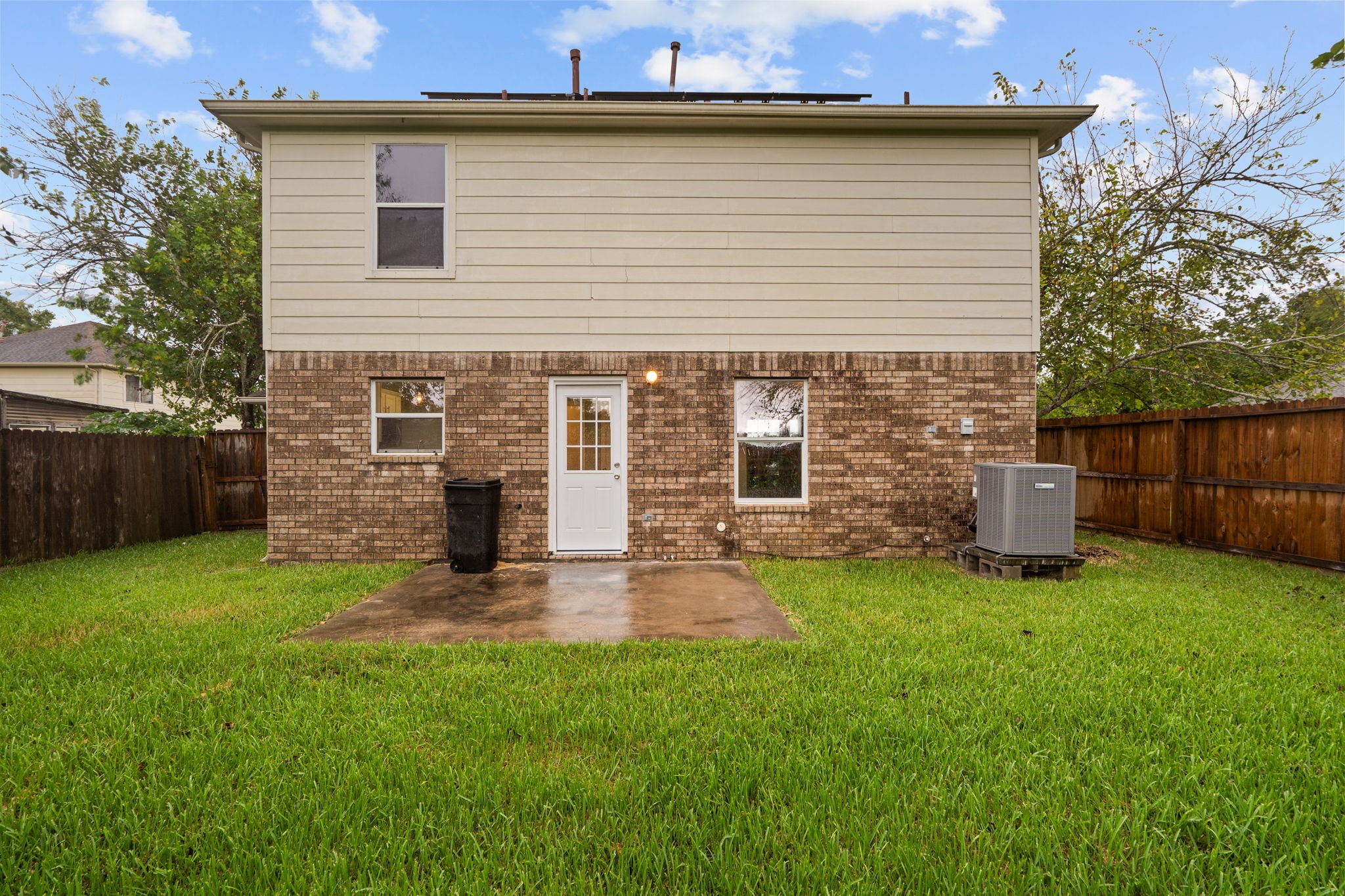 Charming two-story home with a mix of brick and siding exterior, featuring a spacious fenced backyard and a cozy patio area perfect for outdoor gatherings.