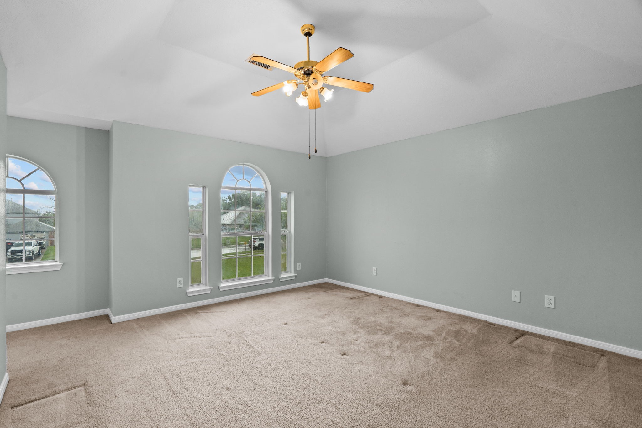 Spacious room with vaulted ceilings, featuring large arched windows that provide ample natural light, complemented by soft carpeting and a ceiling fan for comfort.
