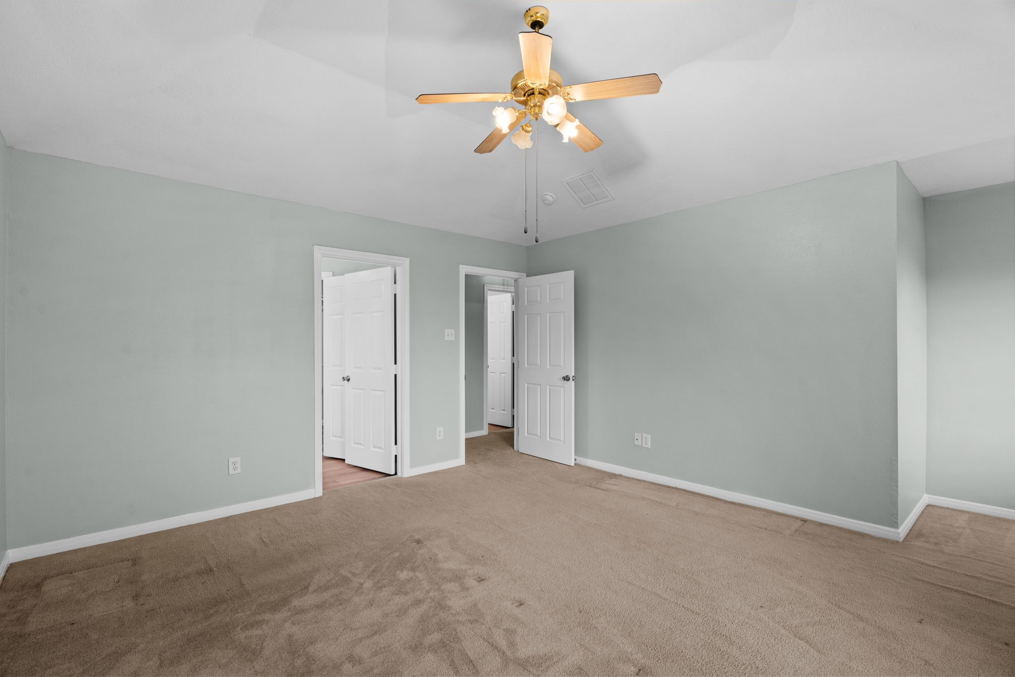 Spacious bedroom with soft green walls, plush carpeting, and a ceiling fan.