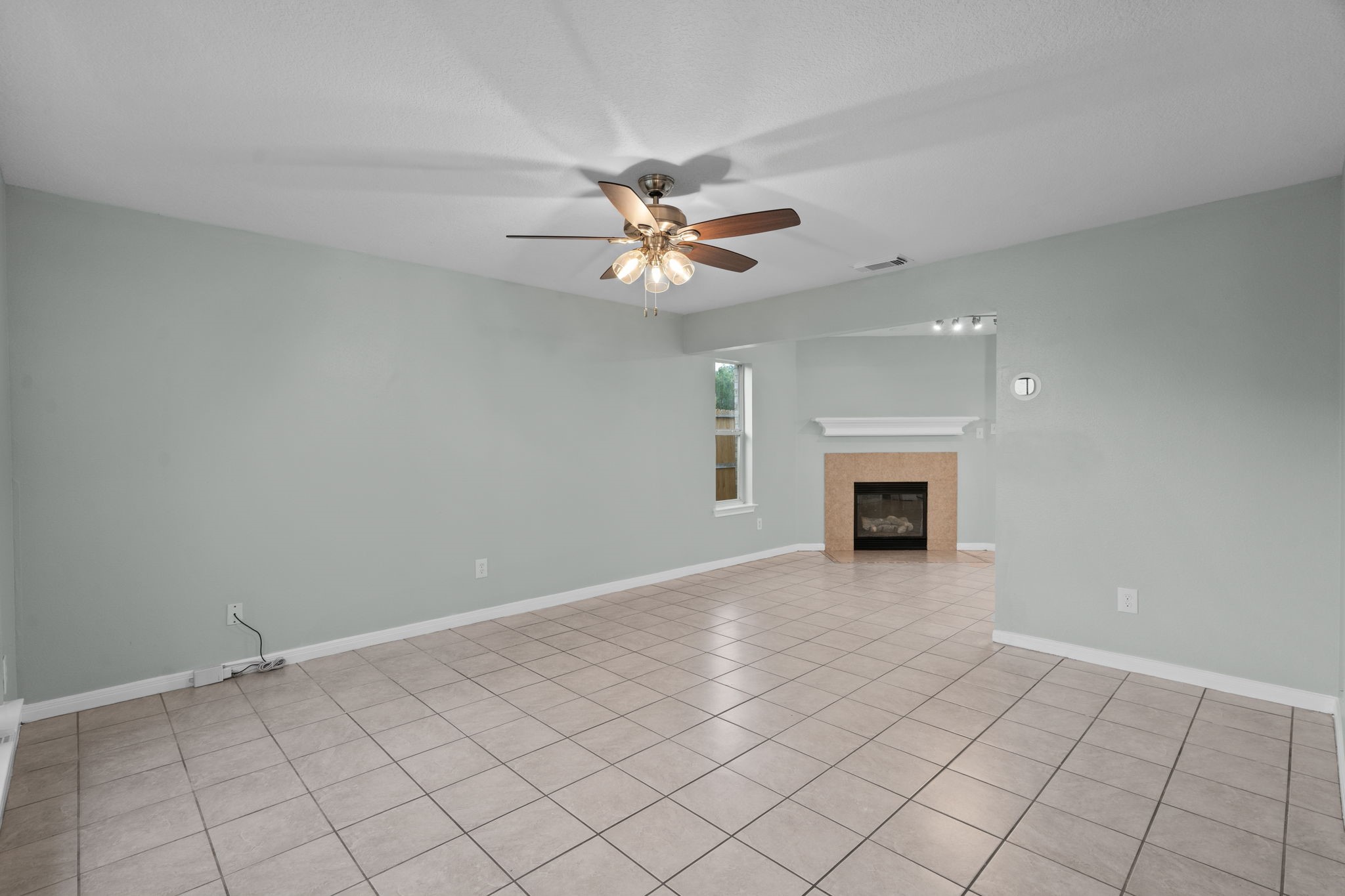 Spacious living area featuring a ceiling fan, fireplace, and large tile flooring, offering a cozy and inviting atmosphere.