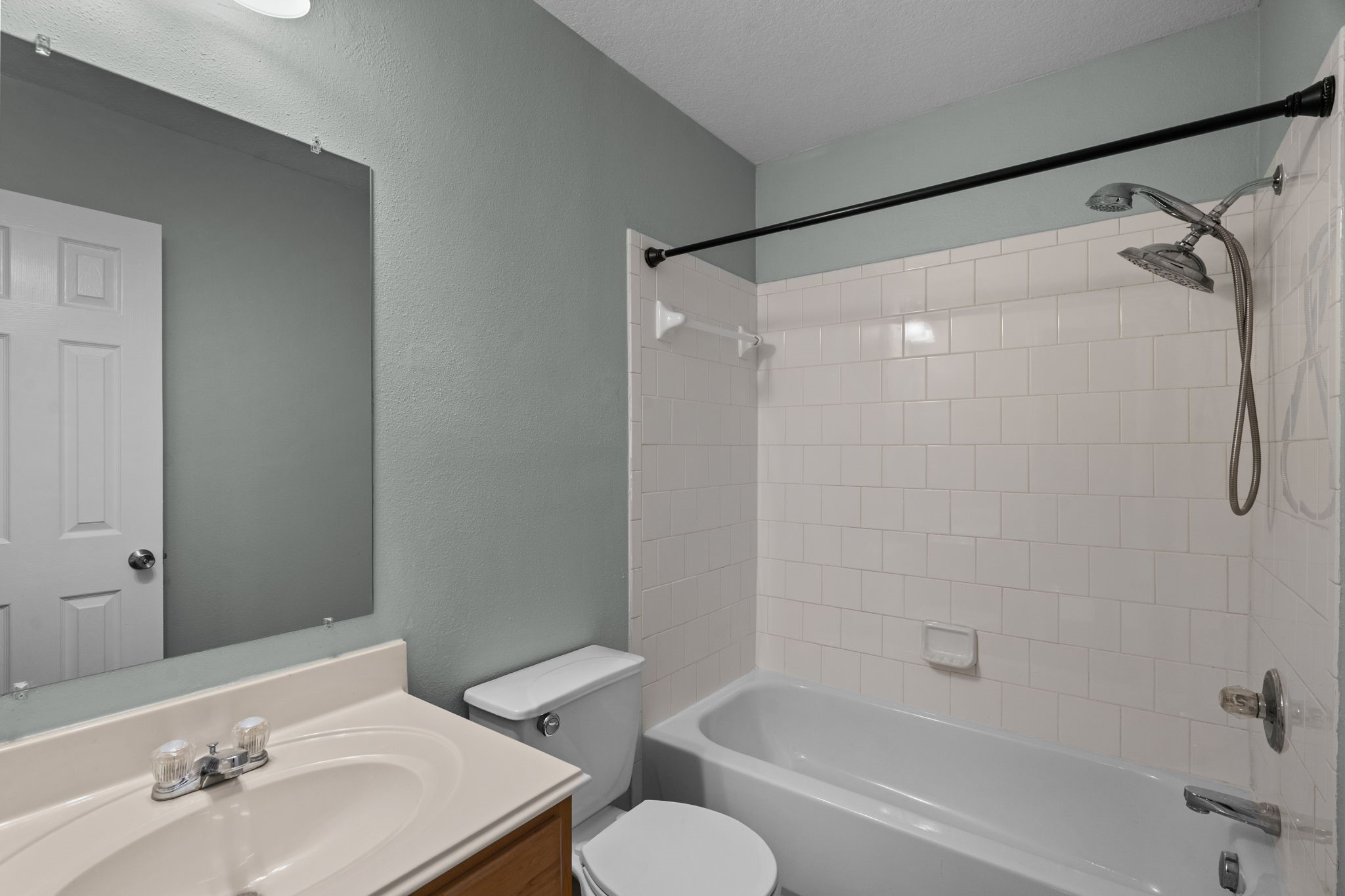 Bright and clean bathroom featuring a classic white tiled shower-tub combo, sleek vanity with ample lighting, and modern fixtures.