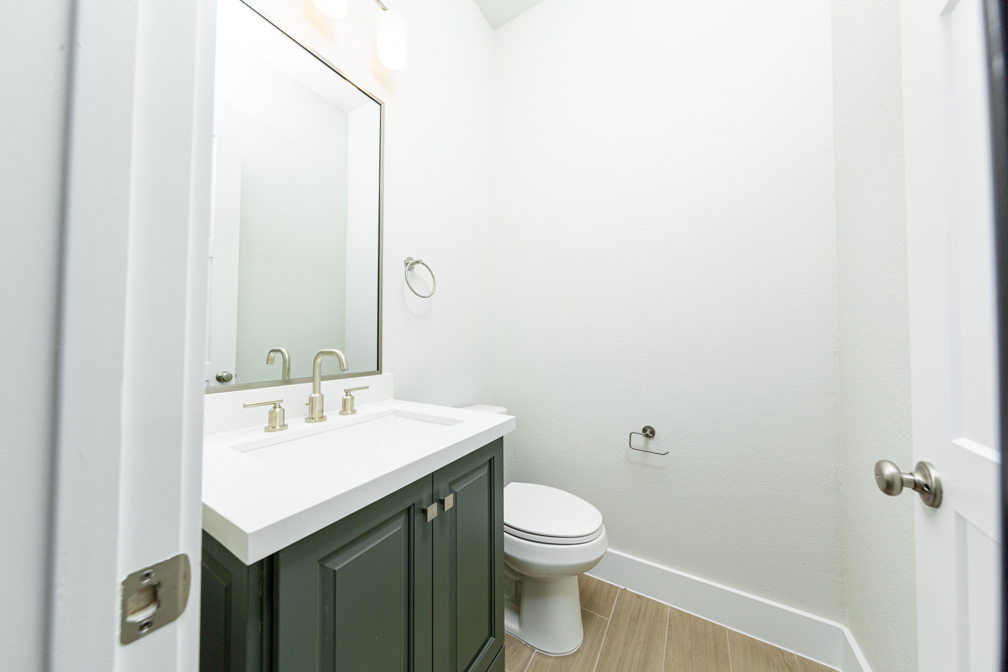 The powder room offers convenience and a modern aesthetic. It features a stained cabinet with quartz countertop and brushed nickel fixtures, matching wall-mounted towel ring, and a simple, large rectangular mirror.