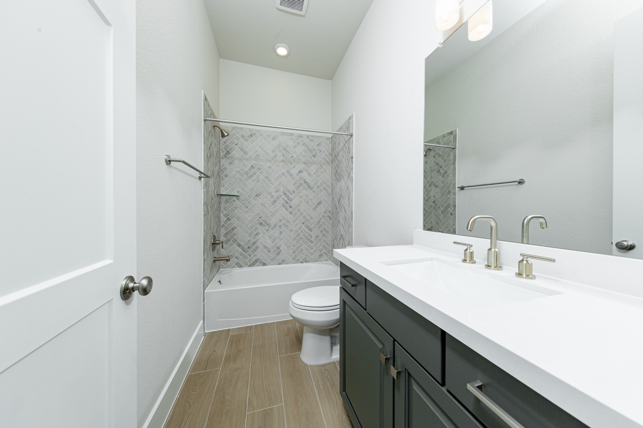 This well-appointed secondary bathroom offers exceptional functionality with its stained cabinet topped with pristine white quartz countertops and undermount sink. Sleek, polished fixtures complement the expansive vanity mirror and chic light vanity fixture.