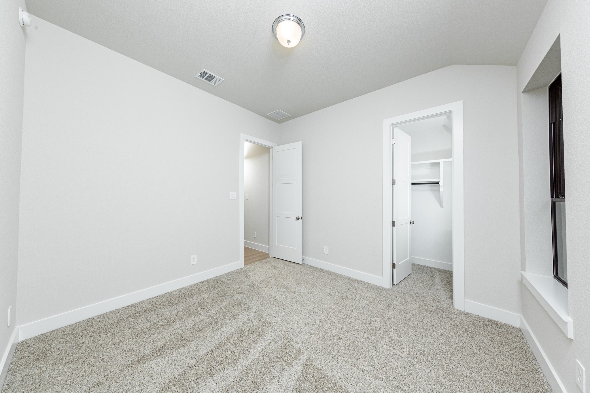 This secondary bedroom offers comfort and style with plush carpeting, neutral paint tones, recessed lighting, large windows, and a walk-in closet.