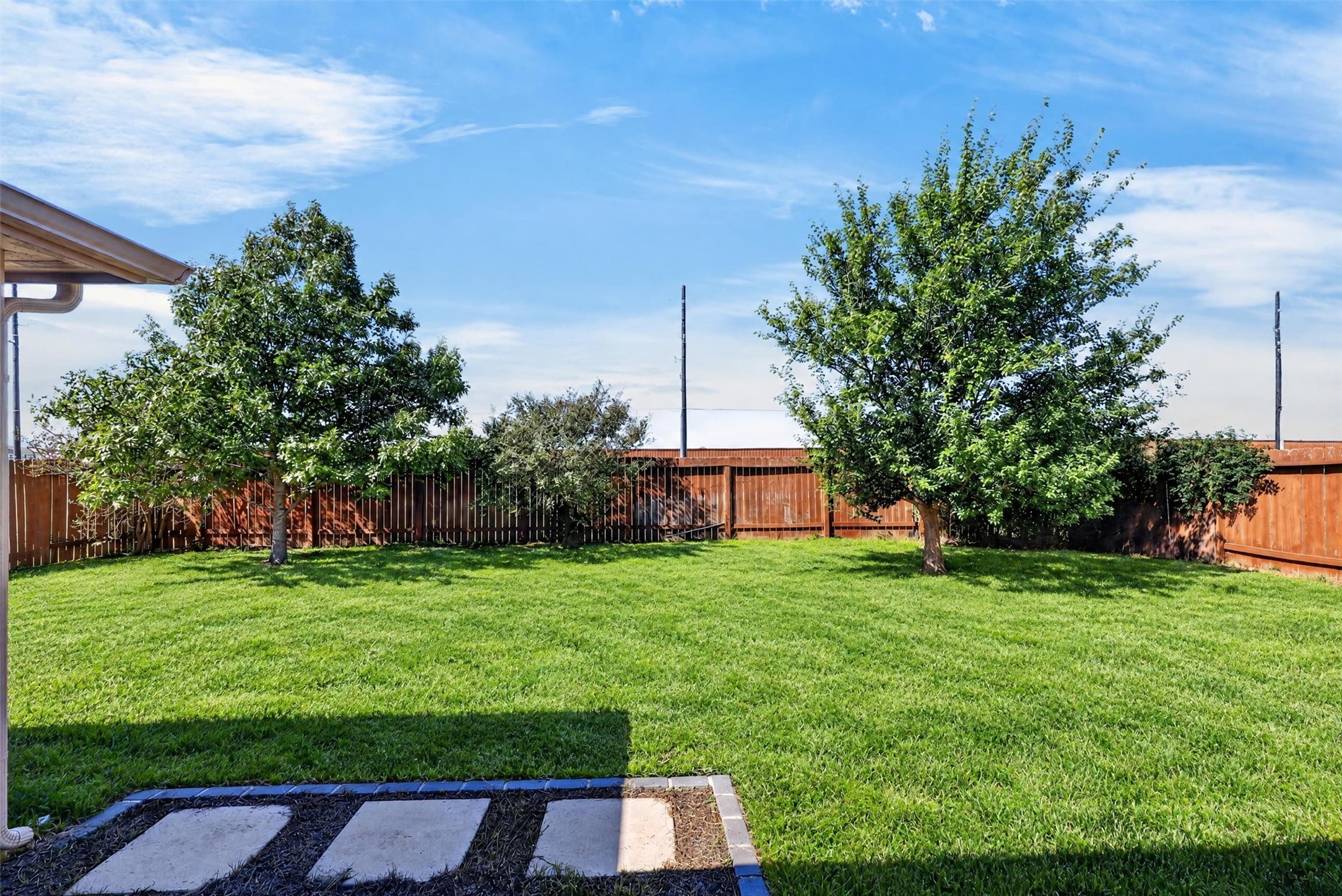 Mature trees frame the spacious, fenced backyard, while the covered patio offers a comfortable setting for morning coffee, evening conversations, or a weekend cookout.