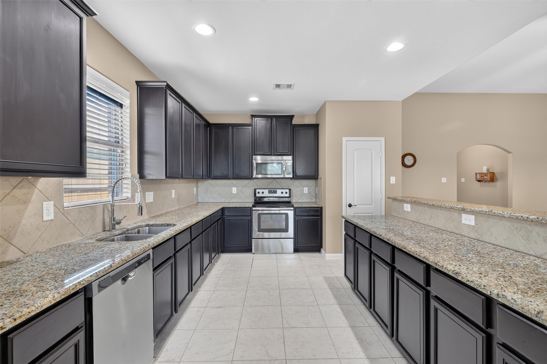 While a stainless-steel refrigerator and dishwasher complement the rich, dark cabinetry. Expansive counters and abundant cabinet storage provide room for meal preparation and everyday essentials. A raised breakfast bar offers space for casual dining and conversation,