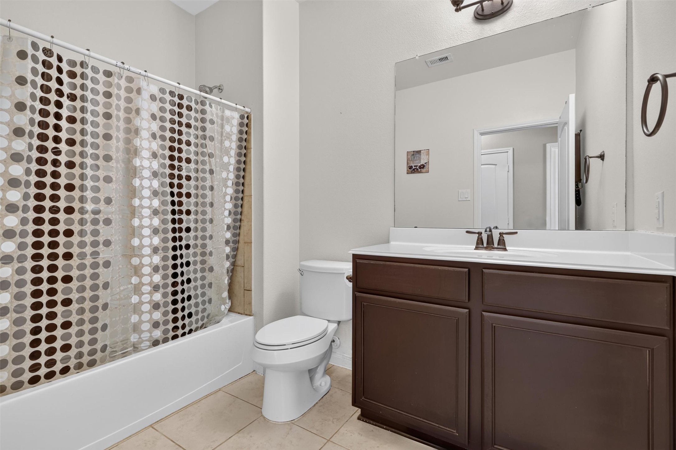 Everyday convenience meets classic style in the second full bathroom. A wide vanity offers generous counter space and cabinet storage, complemented by a large mirror and bronze-toned fixtures. The tub-and-shower combination provides flexibility for a quick rinse or a relaxing soak
