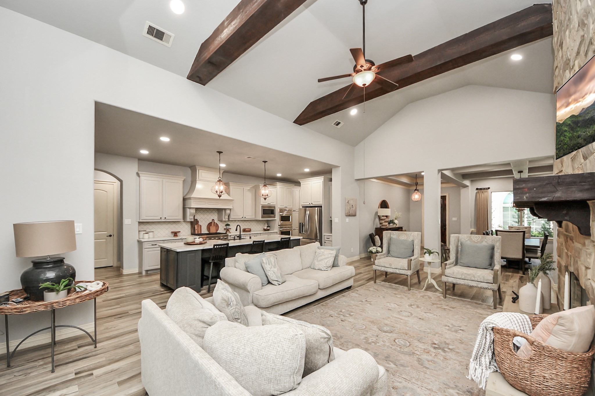 Spacious open-concept living area with vaulted ceilings and exposed beams, featuring a cozy stone fireplace, elegant kitchen with modern appliances, and an inviting dining space perfect for entertaining.