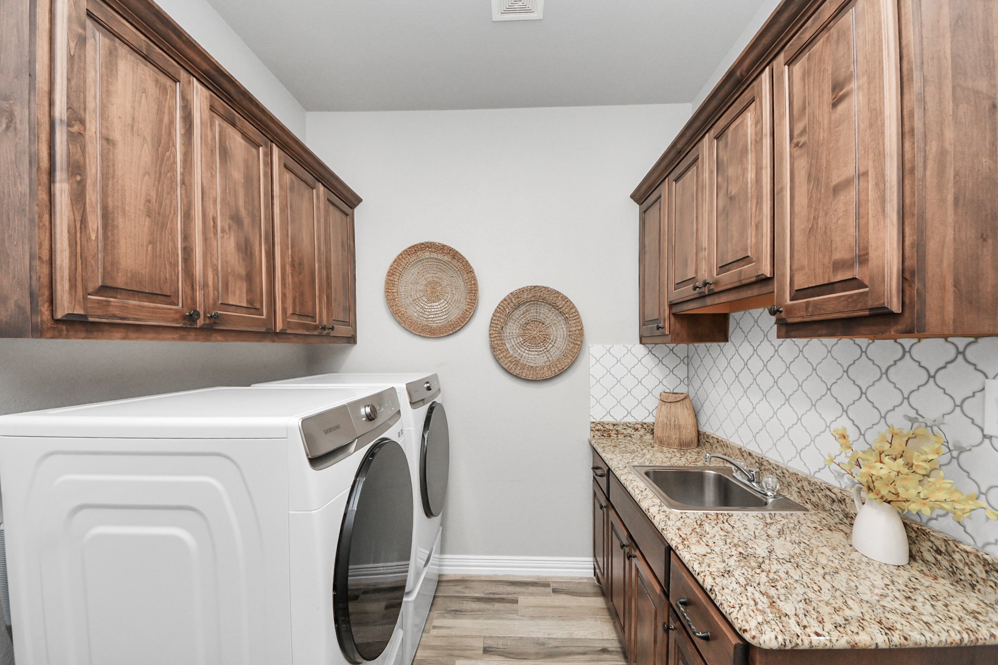 Charming laundry room featuring elegant wood cabinetry, granite countertops, and modern appliances, complemented by stylish backsplash and decorative accents.