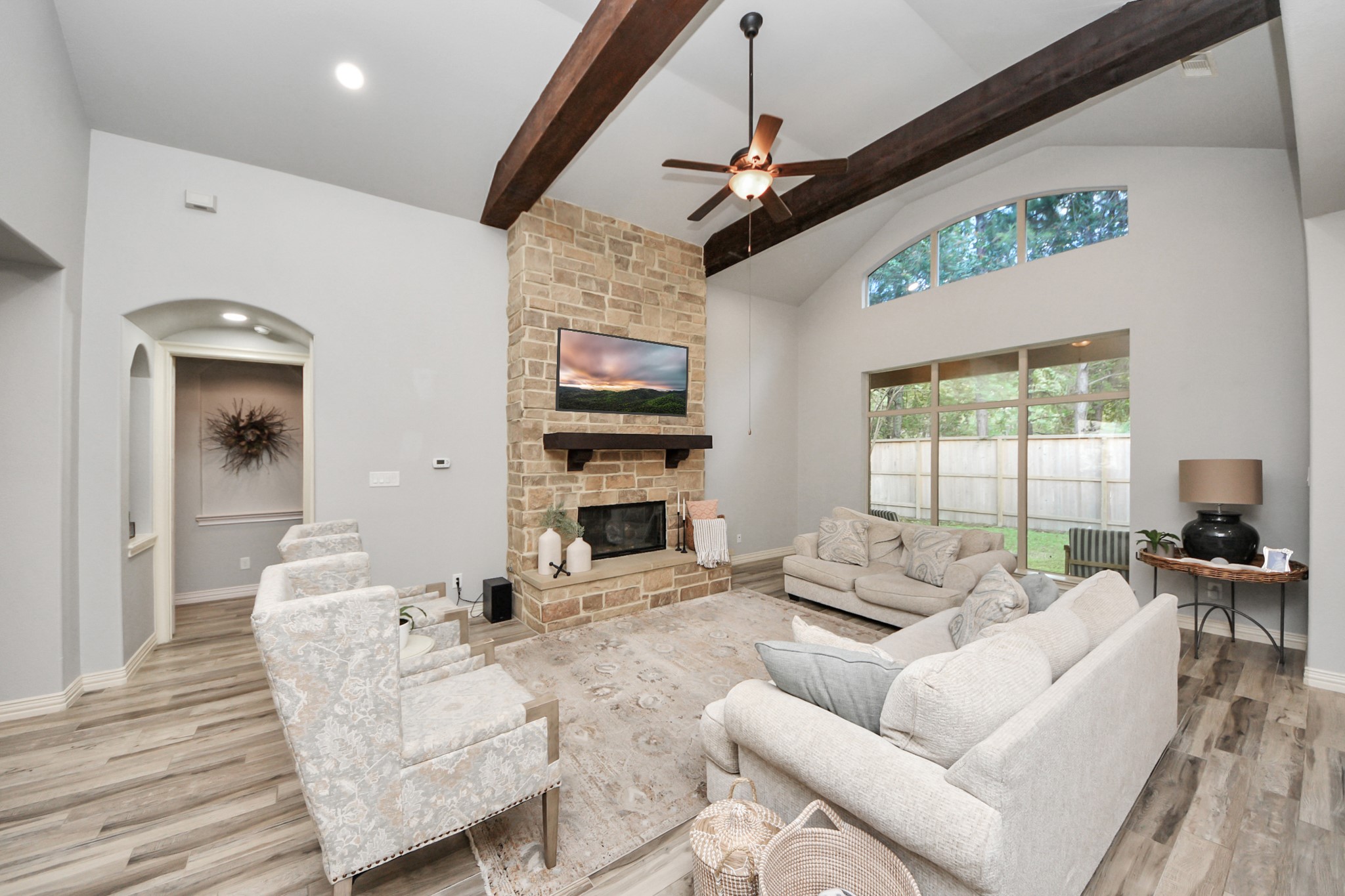 Spacious living room with vaulted ceilings and exposed beams, featuring a stone fireplace and large windows offering abundant natural light.