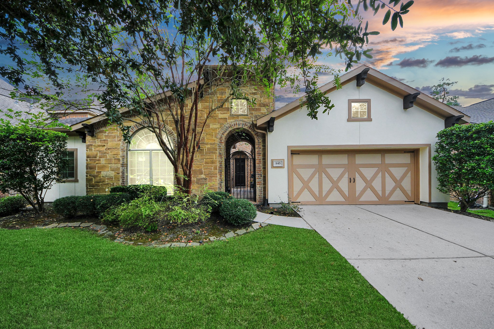 Charming home with a stone-accented facade, elegant arched entryway, and manicured landscaping, complemented by a spacious two-car garage.
