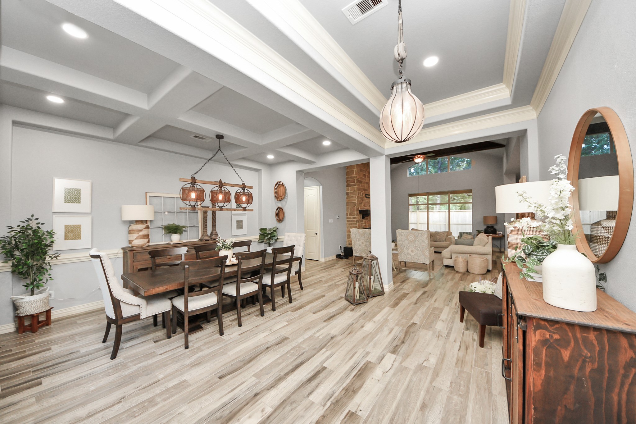 Elegant dining and living area featuring coffered ceilings, stylish light fixtures, and an open layout with a cozy seating area and large windows.