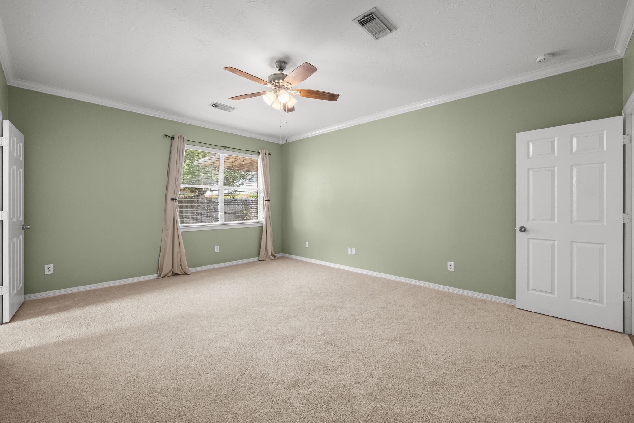 Crown molding adds a refined finishing touch to the expansive primary suite, where new carpeting softens the space and a broad window draws in natural light with a pleasant view of the backyard.