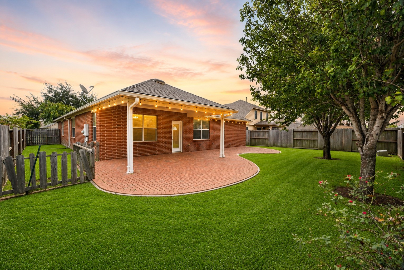 Extending beneath the home's original roofline, the covered patio offers a substantial shaded setting for outdoor dining, casual gatherings, or simply unwinding beside the green lawn.