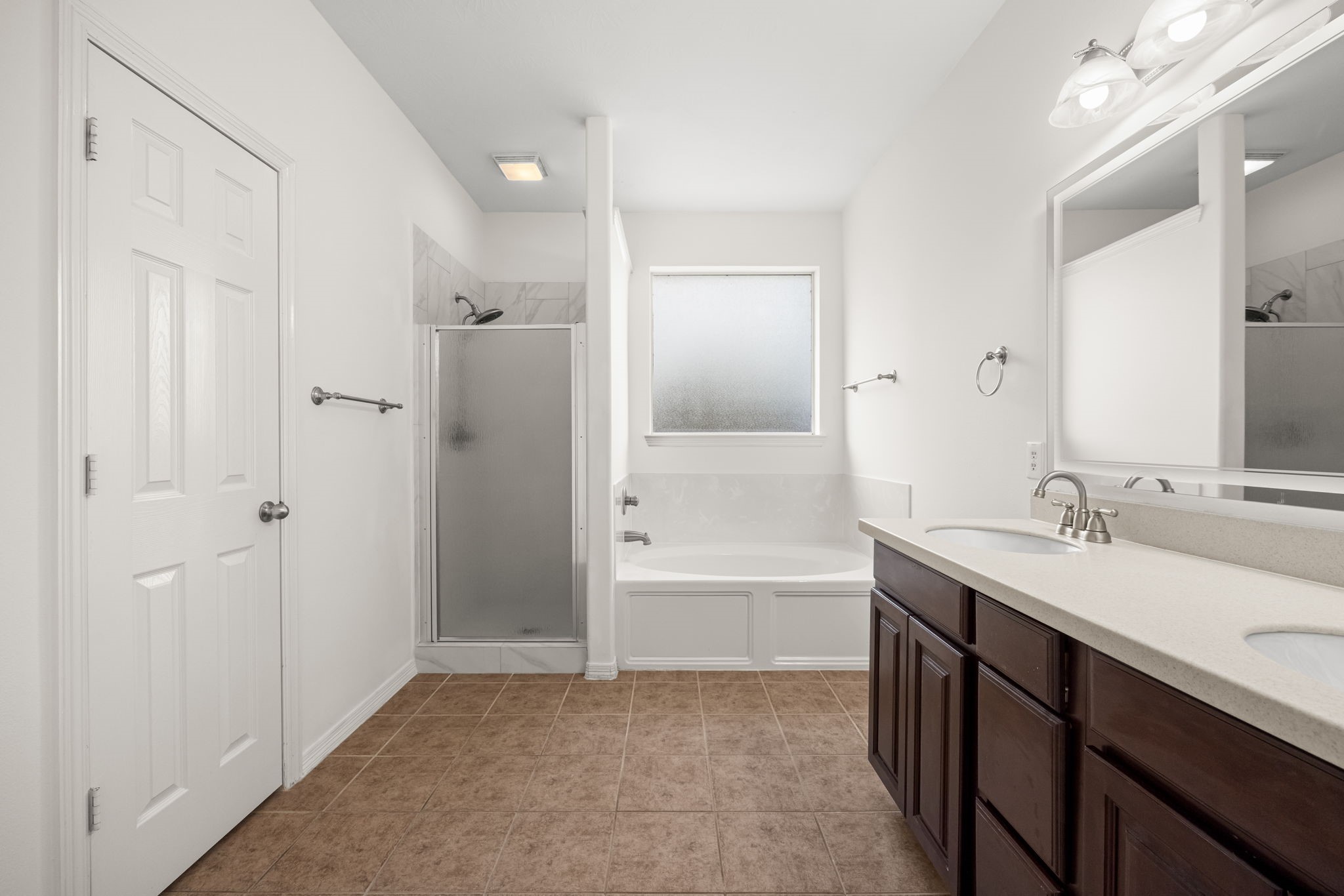 The primary bath offers a generous dual-sink vanity, a deep soaking tub beneath frosted privacy glass, and a separate enclosed shower, providing distinct spaces for a quick morning routine or a longer evening soak.