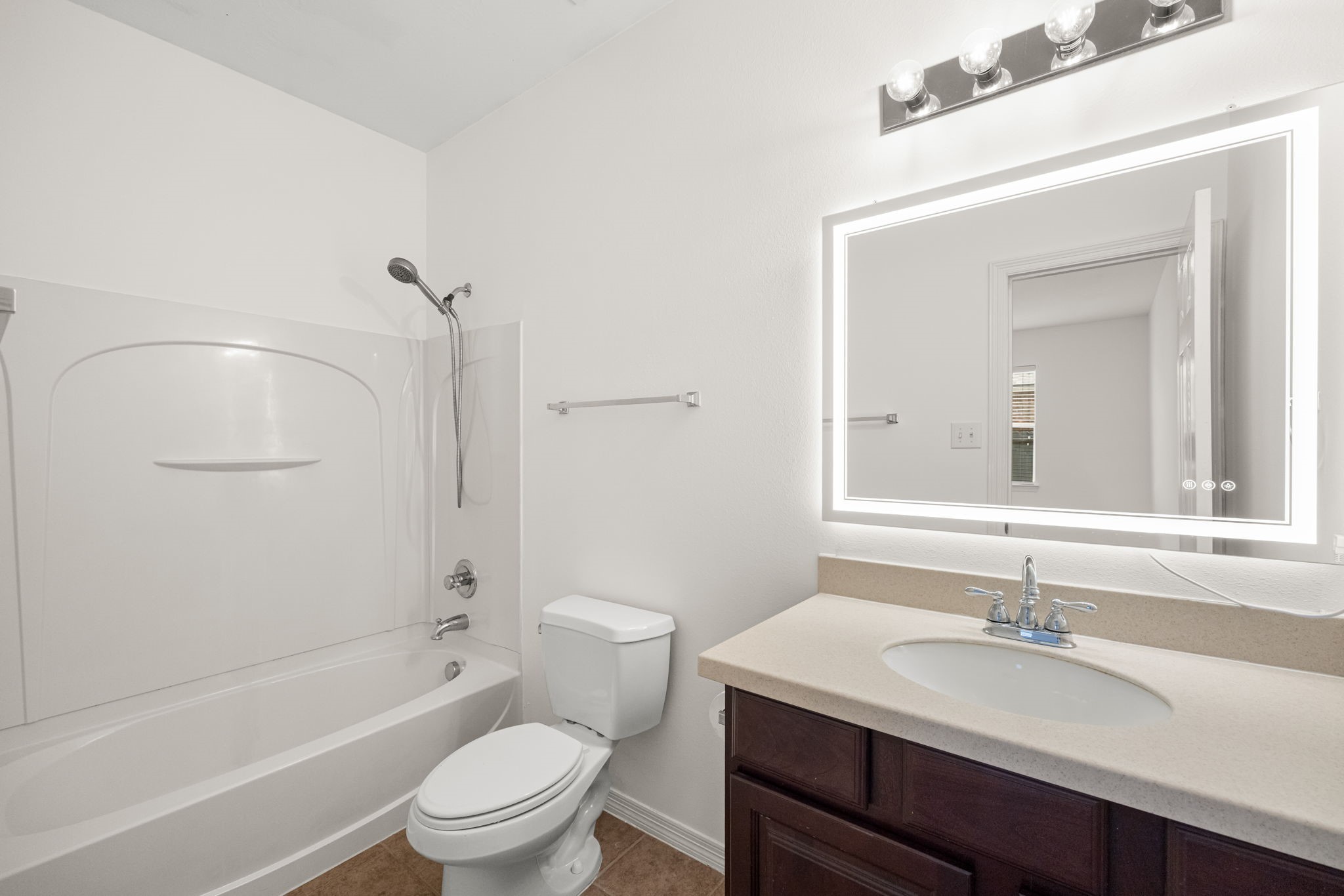 The secondary bathroom features a vanity, a well-lit mirror, and a tub-shower combination, bringing the everyday essentials together in a practical arrangement.