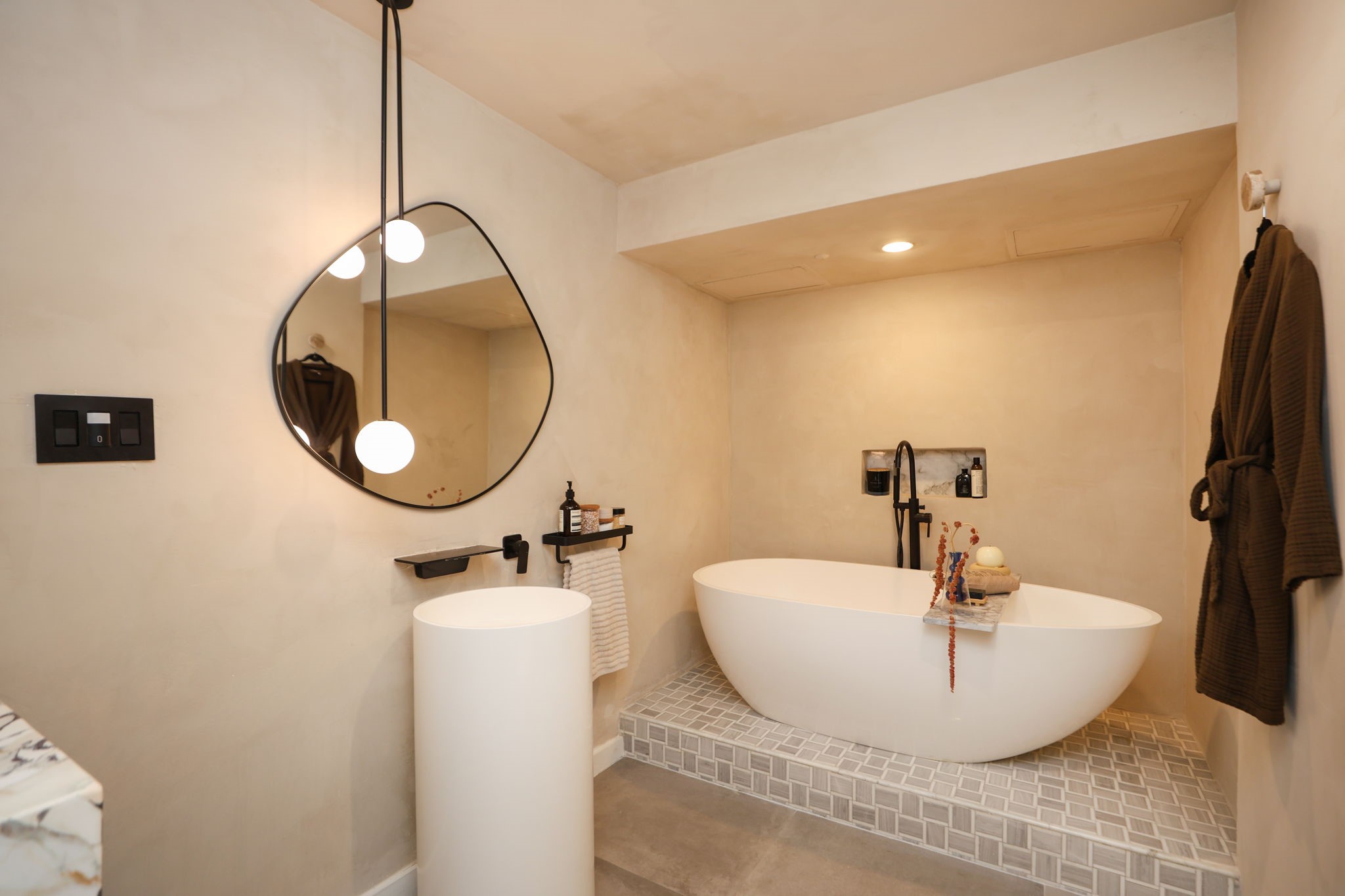 Spa-inspired first floor bath featuring a freestanding soaking tub elevated on a mosaic-tile platform with black matte fixtures and built-in niche.