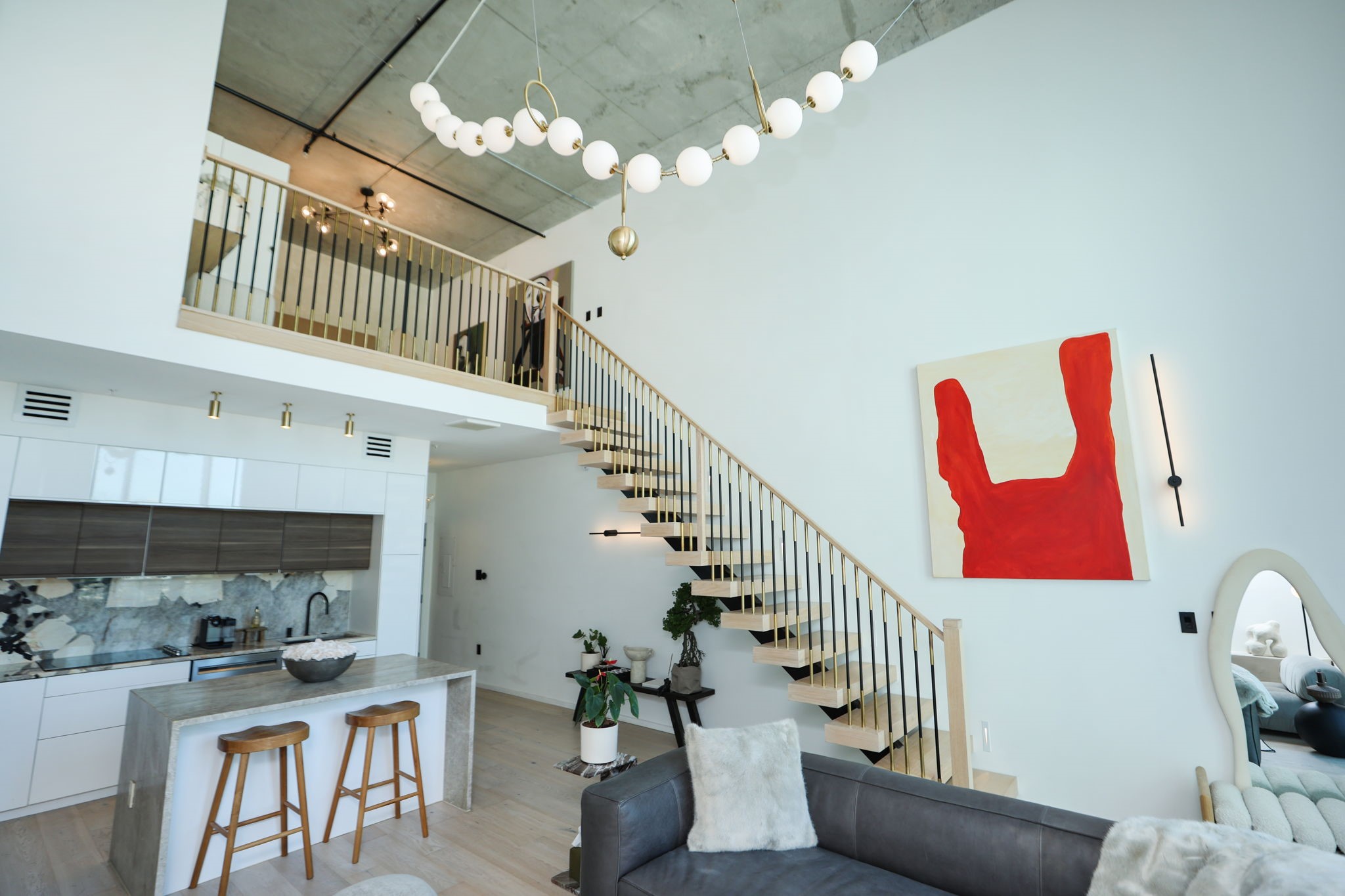Soaring ceilings, a floating staircase, and statement pendant chandelier give this loft its dramatic gallery-like feel, with the primary bedroom on the second floor.