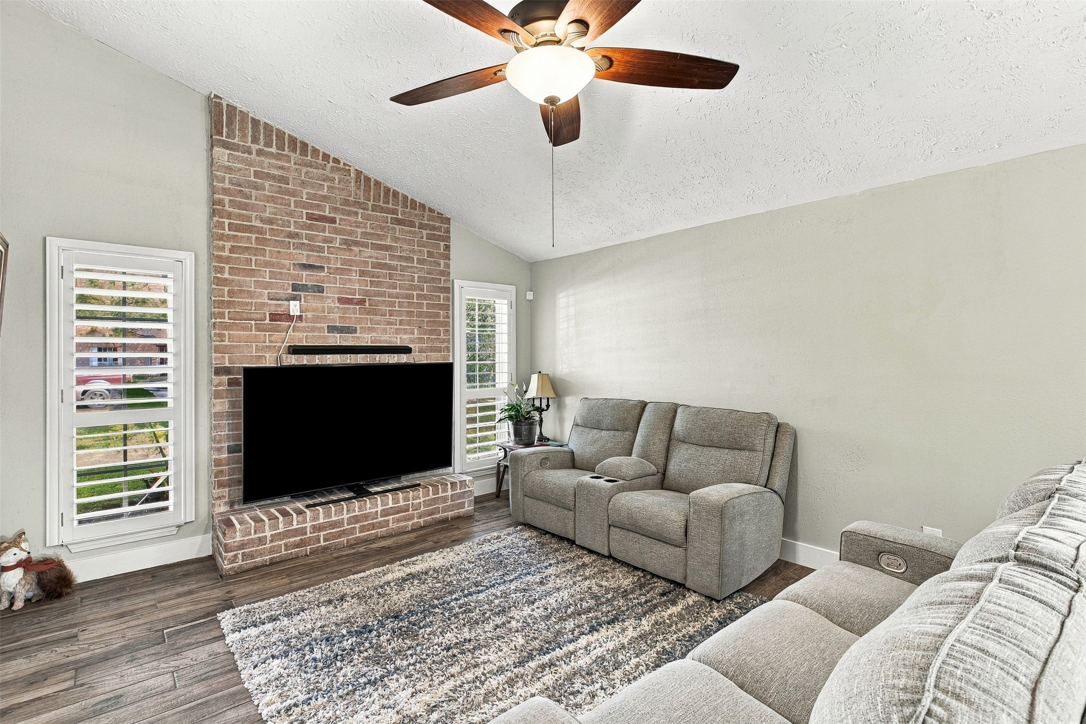 Inviting living room featuring brick fireplace abundant natural light, and plantation shutters.