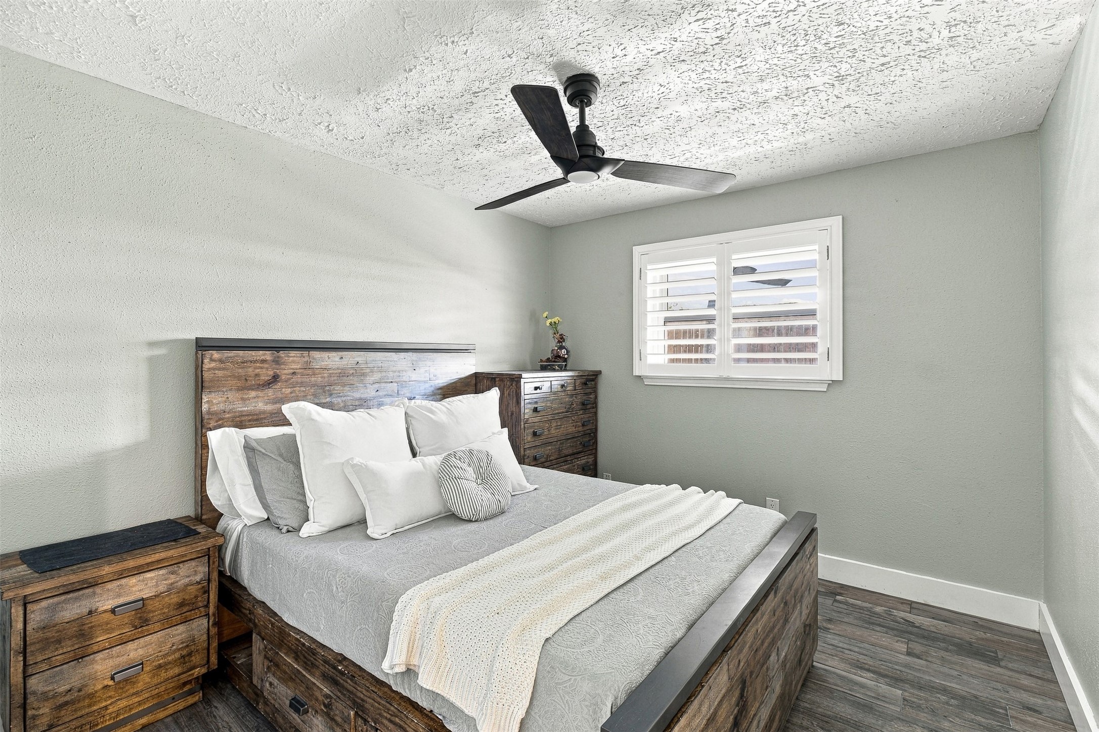 Bright secondary bedroom with updated porcelain tile flooring, modern ceiling fan, plantation shutters, and plenty of natural light.