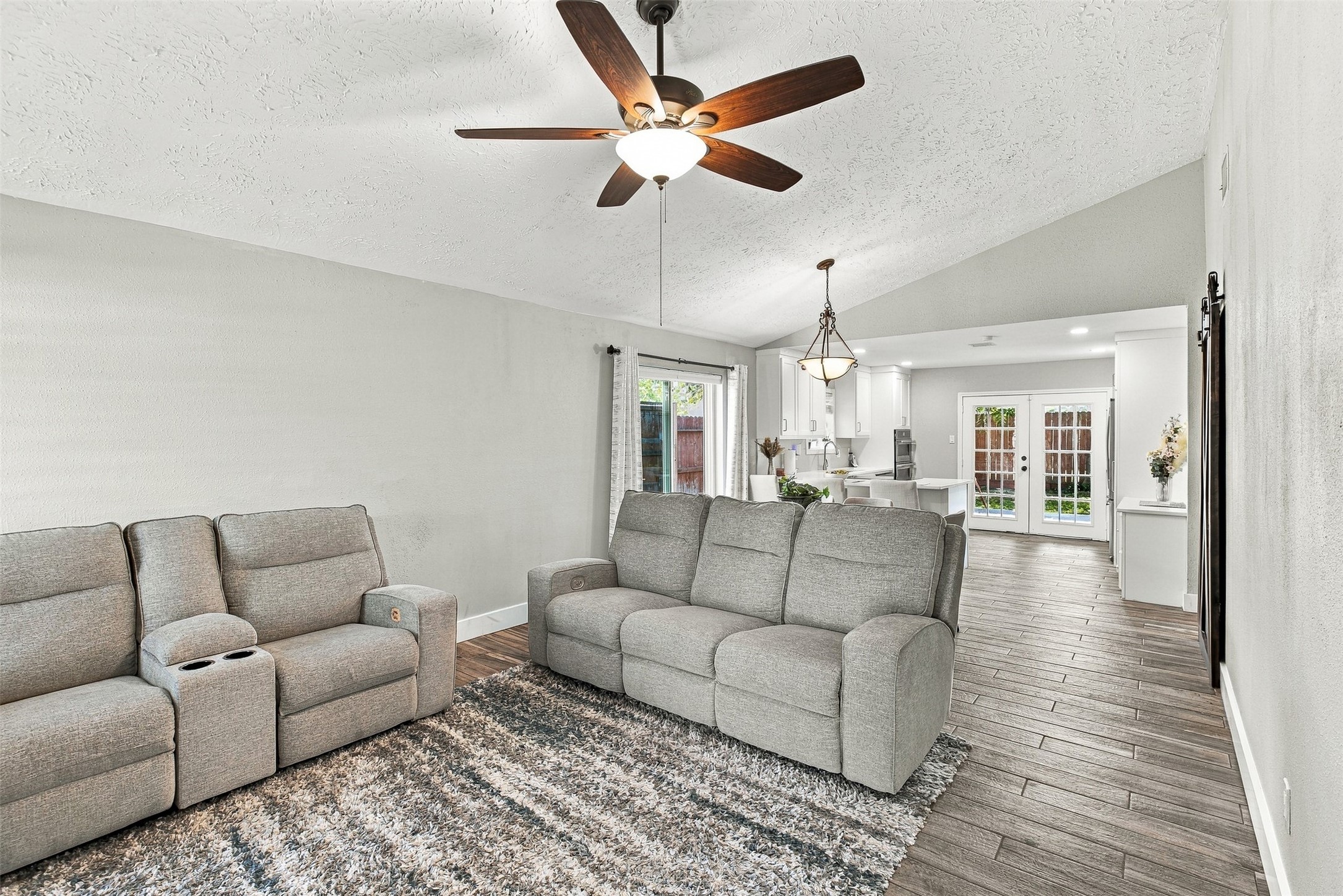 Spacious living area with vaulted ceiling, updated flooring, ceiling fan, and an open flow into the dining and kitchen areas.