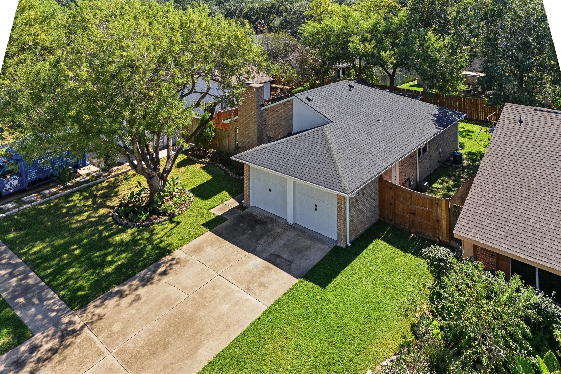 Aerial view showcases the home's roofline, two-car garage, mature trees, and established homesite.