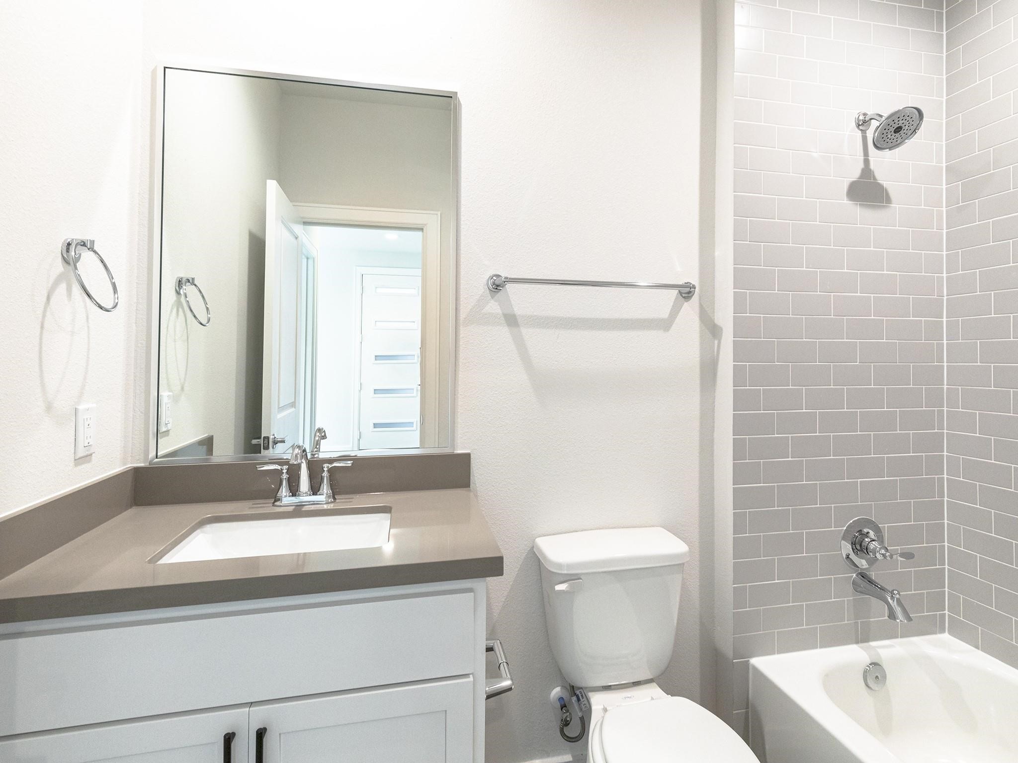 Modern secondary bathroom featuring a sleek vanity with a large mirror, a tiled shower-tub combo, and contemporary fixtures.

Note: Photos 2022
