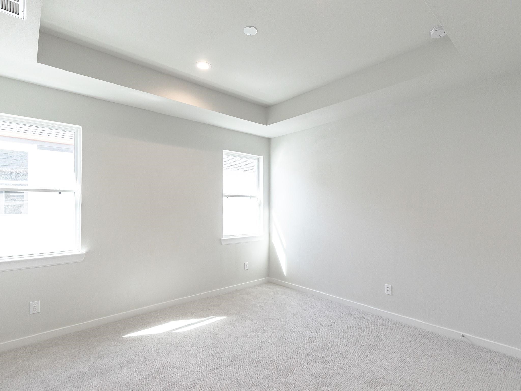 Bright and spacious primary bedroom featuring a tray ceiling, plush carpeting, and ample natural light from two windows.
Note: Photos 2022 Bright and spacious primary bedroom featuring a tray ceiling, plush carpeting, and ample natural light from two windows.
Note: Photos 2022