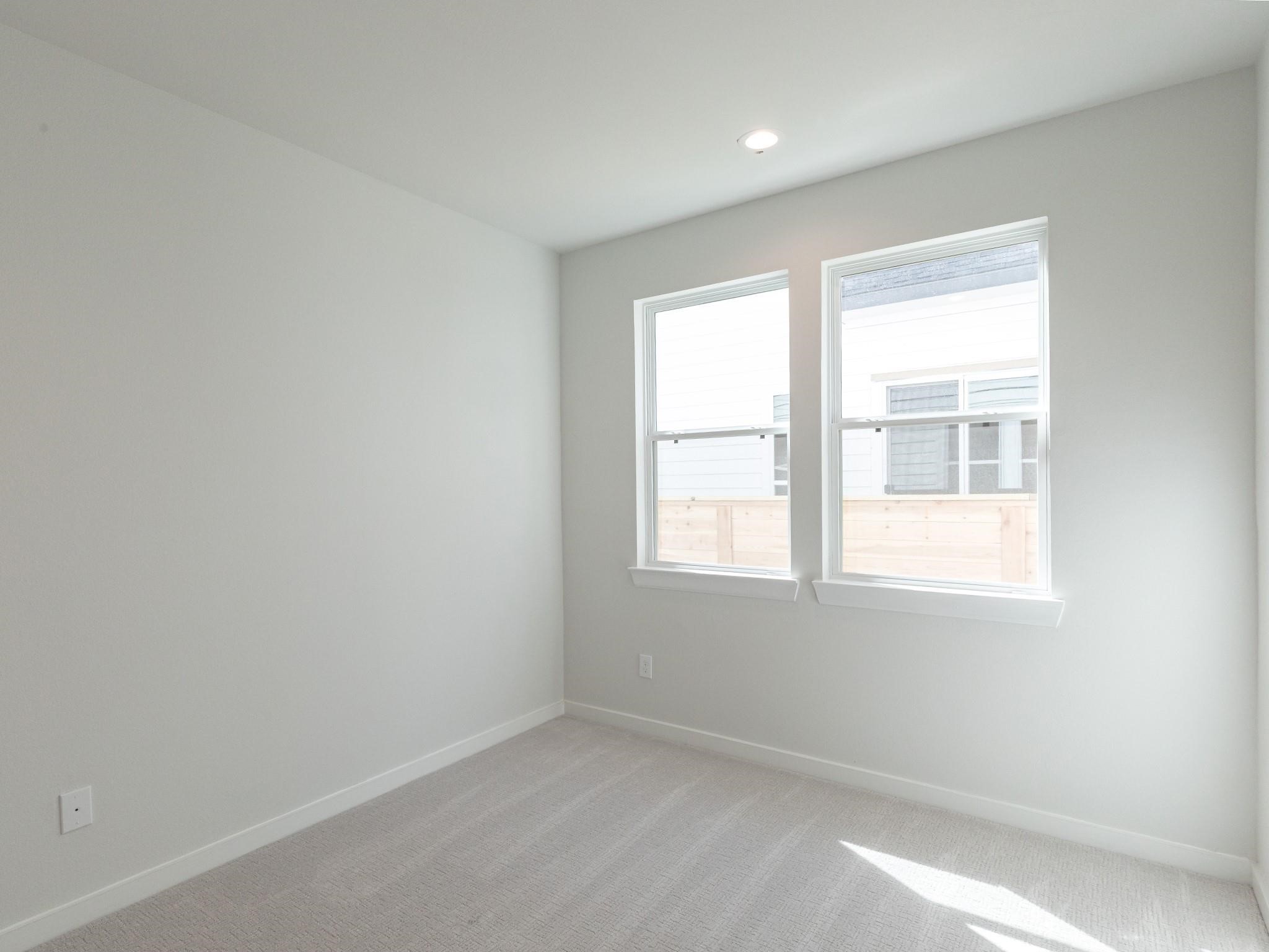 Bright and airy secondary bedroom with neutral walls, plush carpeting, and two large windows inviting natural light.

Note: Photos 2022
