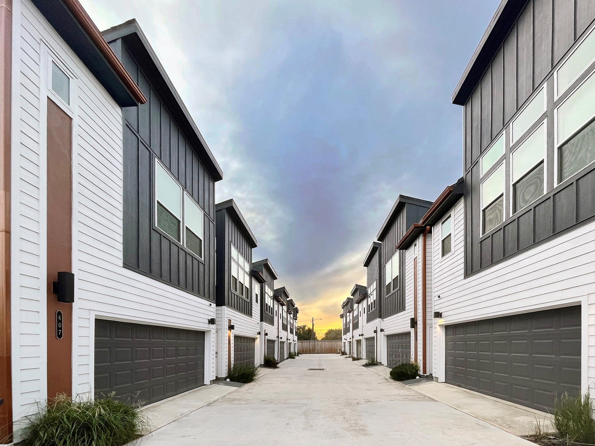 Modern homes with sleek black-and-white exteriors line a private driveway, offering spacious garages and contemporary design in a peaceful setting. Note: Photos 2022