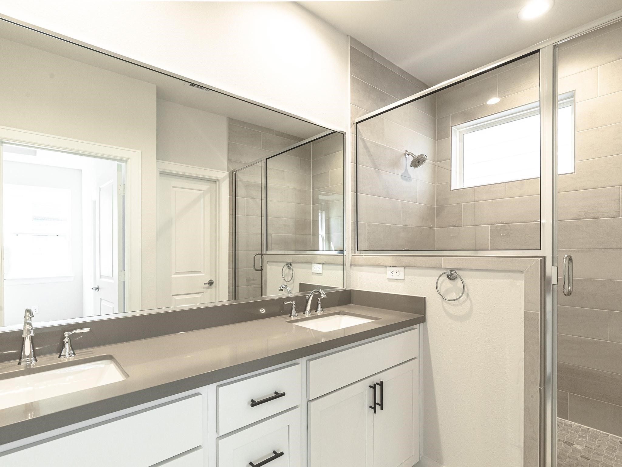 Modern primary bathroom featuring a spacious dual-sink vanity with sleek fixtures and a glass-enclosed shower, highlighted by elegant tile work and ample natural light.

Note: Photos 2022