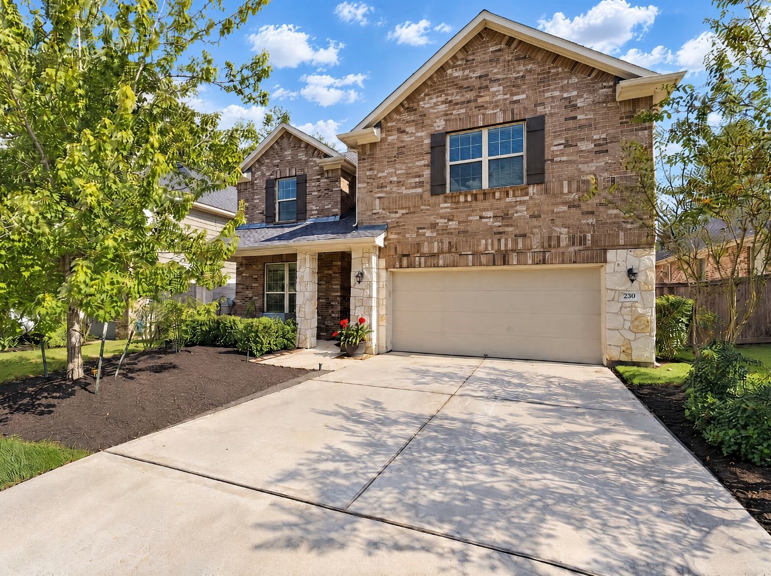 Stately two-story home with a brick and stone faade, dark shutters, and a covered front entry. A two-car garage and wide concrete driveway pair with landscaped mulch beds for solid curb appeal.
This photo has been digitally staged to illustrate the possibilities of the homes aesthetic and potential design. Some furnishings and dcor shown are for visual inspiration.