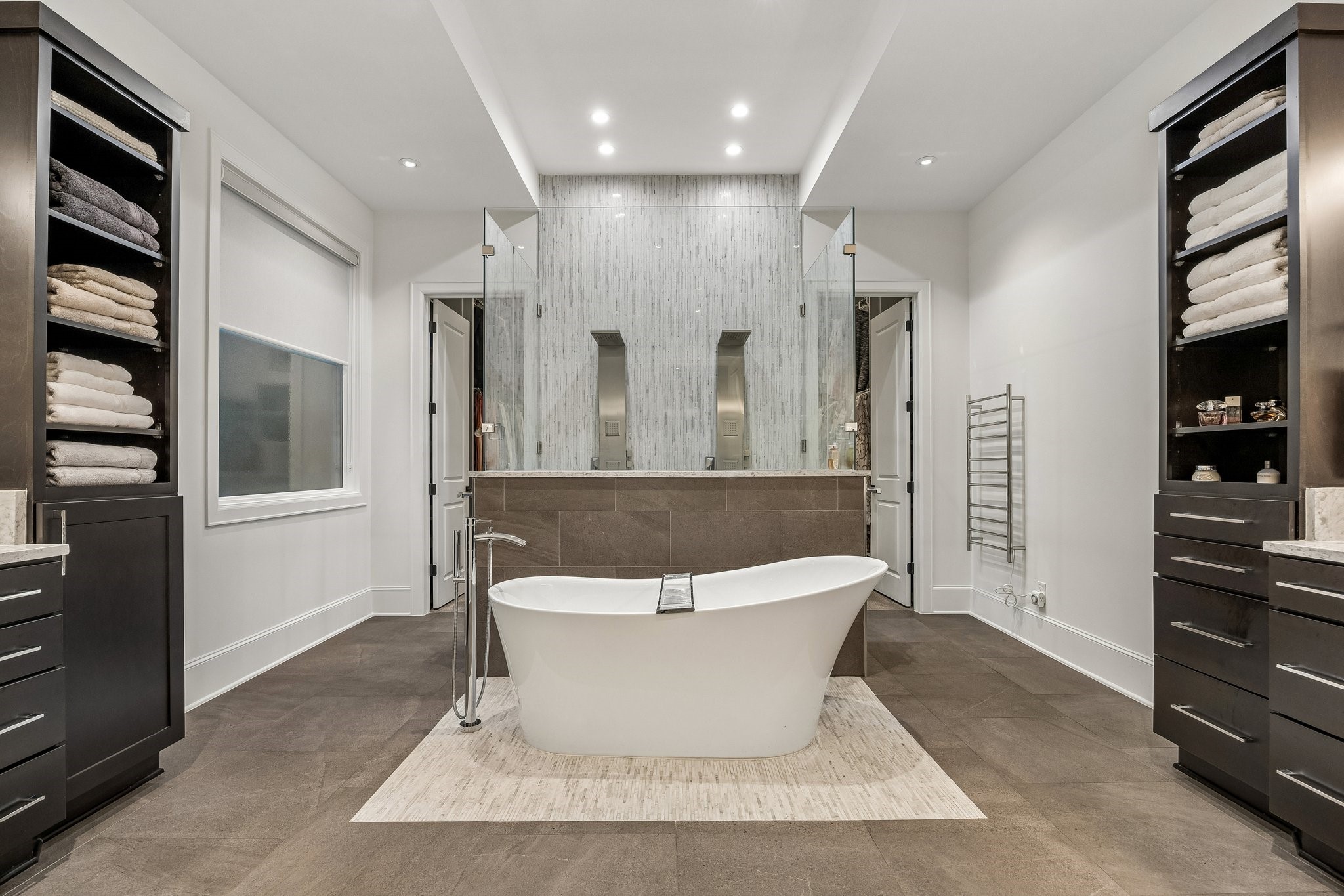 This extraordinary primary bathroom is a stunning expression of contemporary luxury, showcasing sophisticated architectural design, exquisite finishes, and a beautifully balanced, spa-inspired atmosphere. The expansive layout features a striking freestanding soaking tub positioned as the room's dramatic centerpiece, creating an inviting sanctuary for relaxation and rejuvenation.