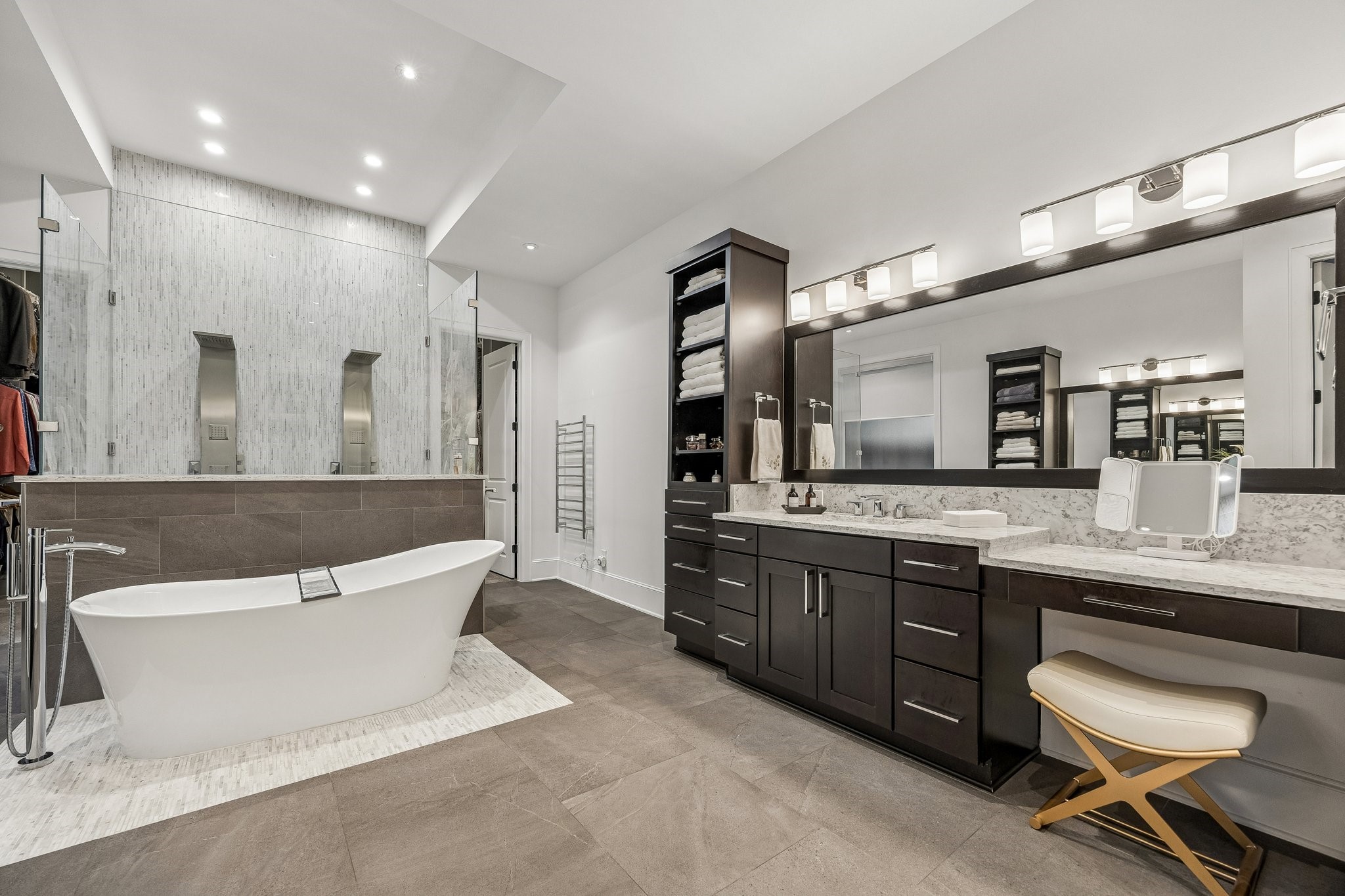 Rich charcoal-toned tile flooring provides a beautiful contrast to the Classic Carrara Stone Counters.  Shaker Style Cabinetry, vanity, pendent lighting, tons of linen storgae and open shelving.  There is also a towel warmer conveniently located outside the shower.