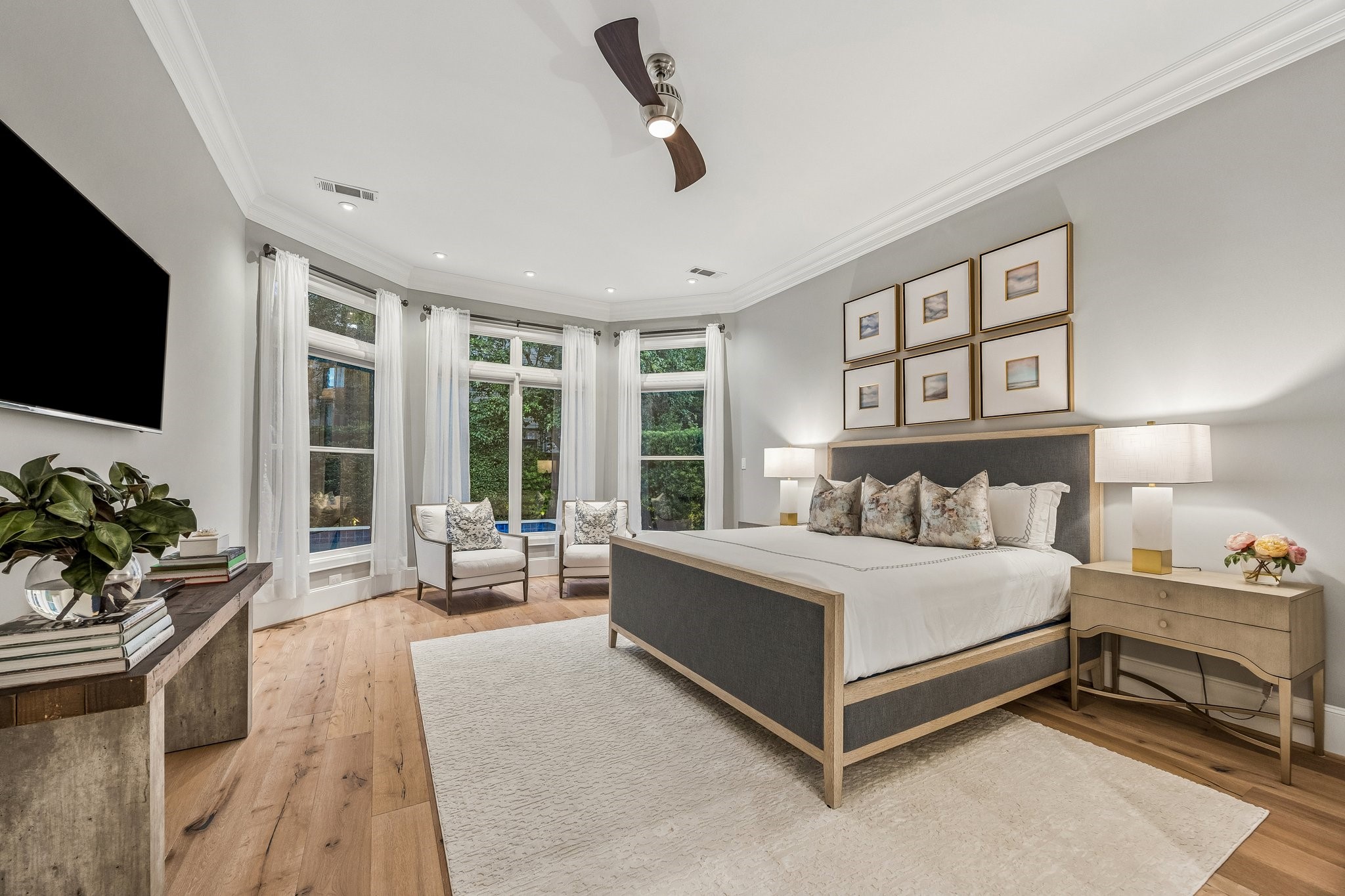 Generously proportioned Primary Suite with a stunning curved wall of expansive windows.  LED recessed lighting, wide plank floors, crown molding, 8 Inch baseboards, Linear ceiling fan, and window treatments.